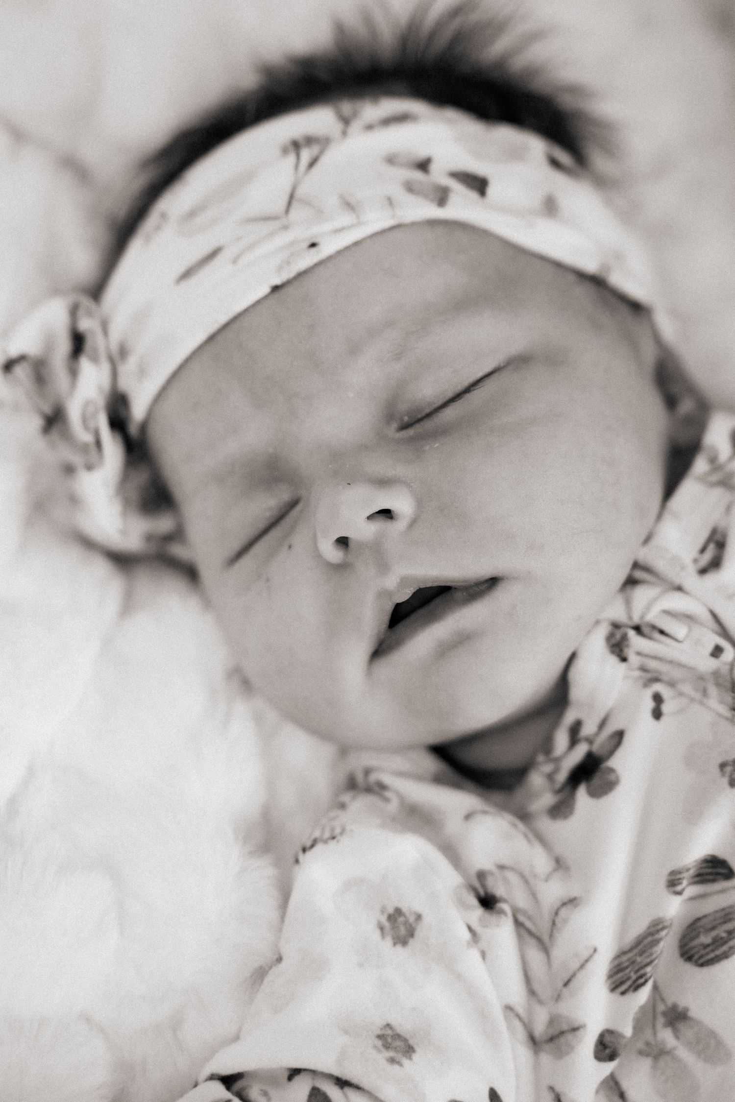 Sleeping newborn baby wearing a floral outfit and headband in black and white portrait.