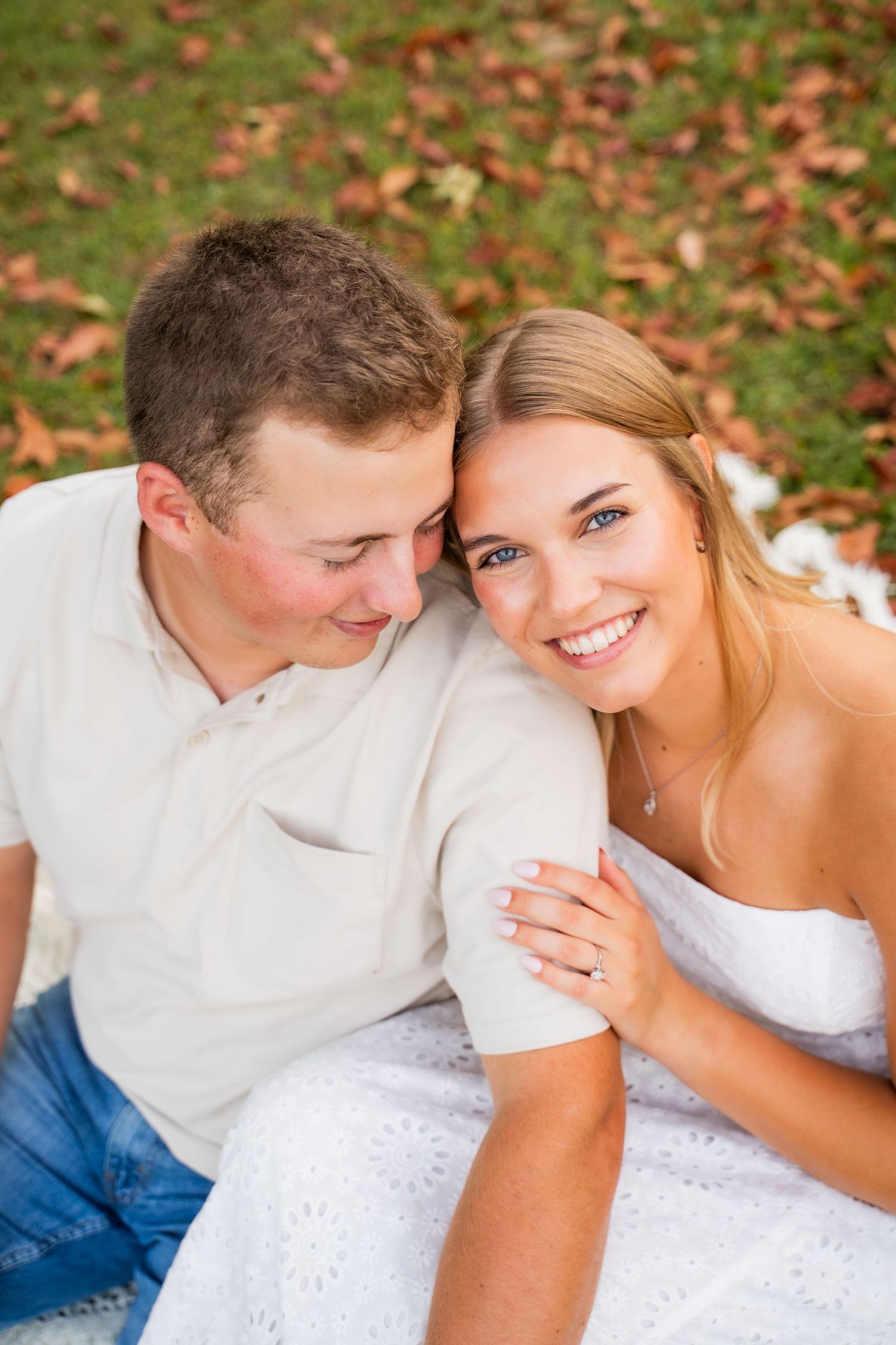 Romantic autumn engagement photos on grass with fallen leaves.