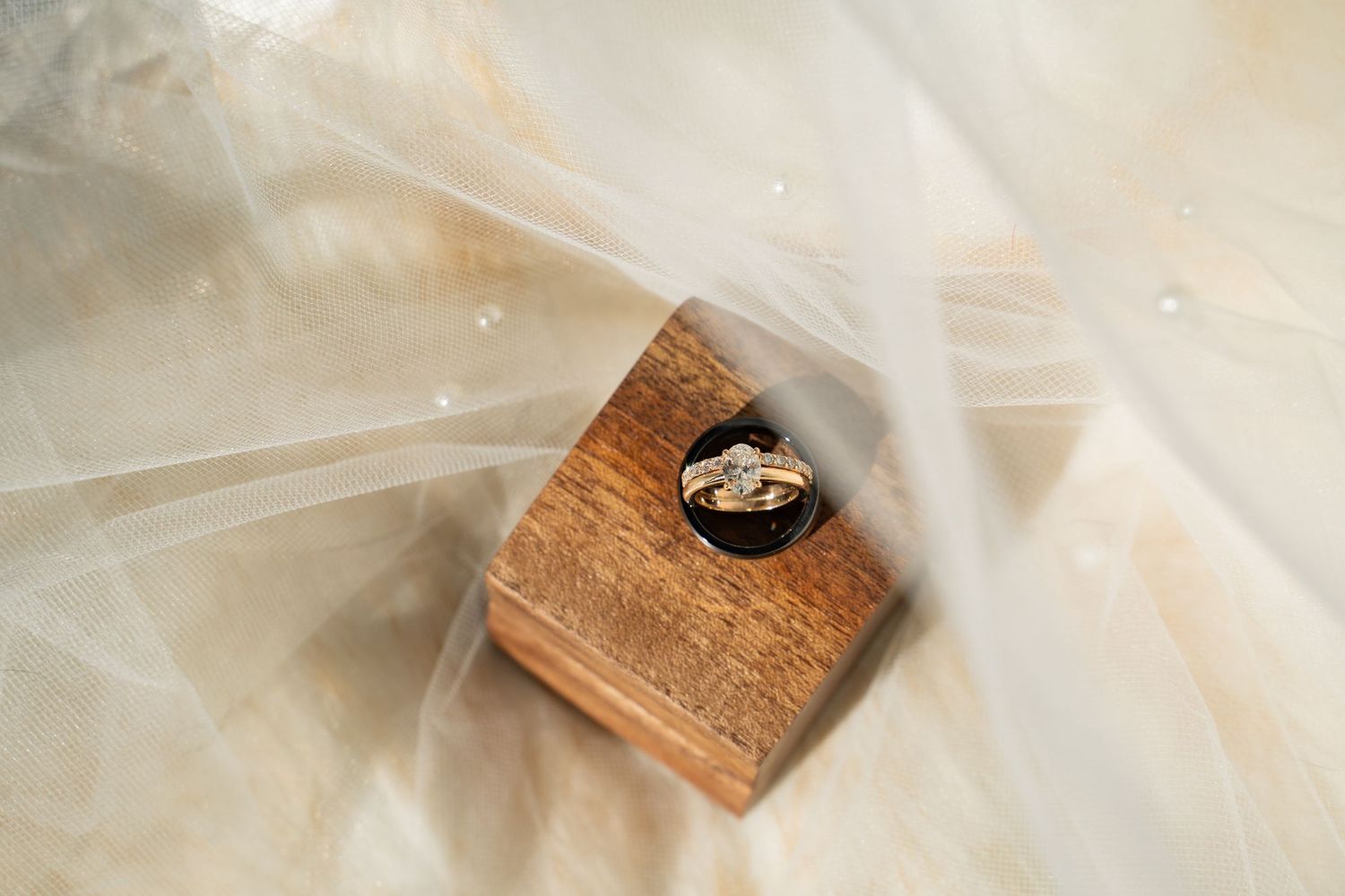 Wedding rings nestled in a small wooden box wrapped in delicate tulle fabric.