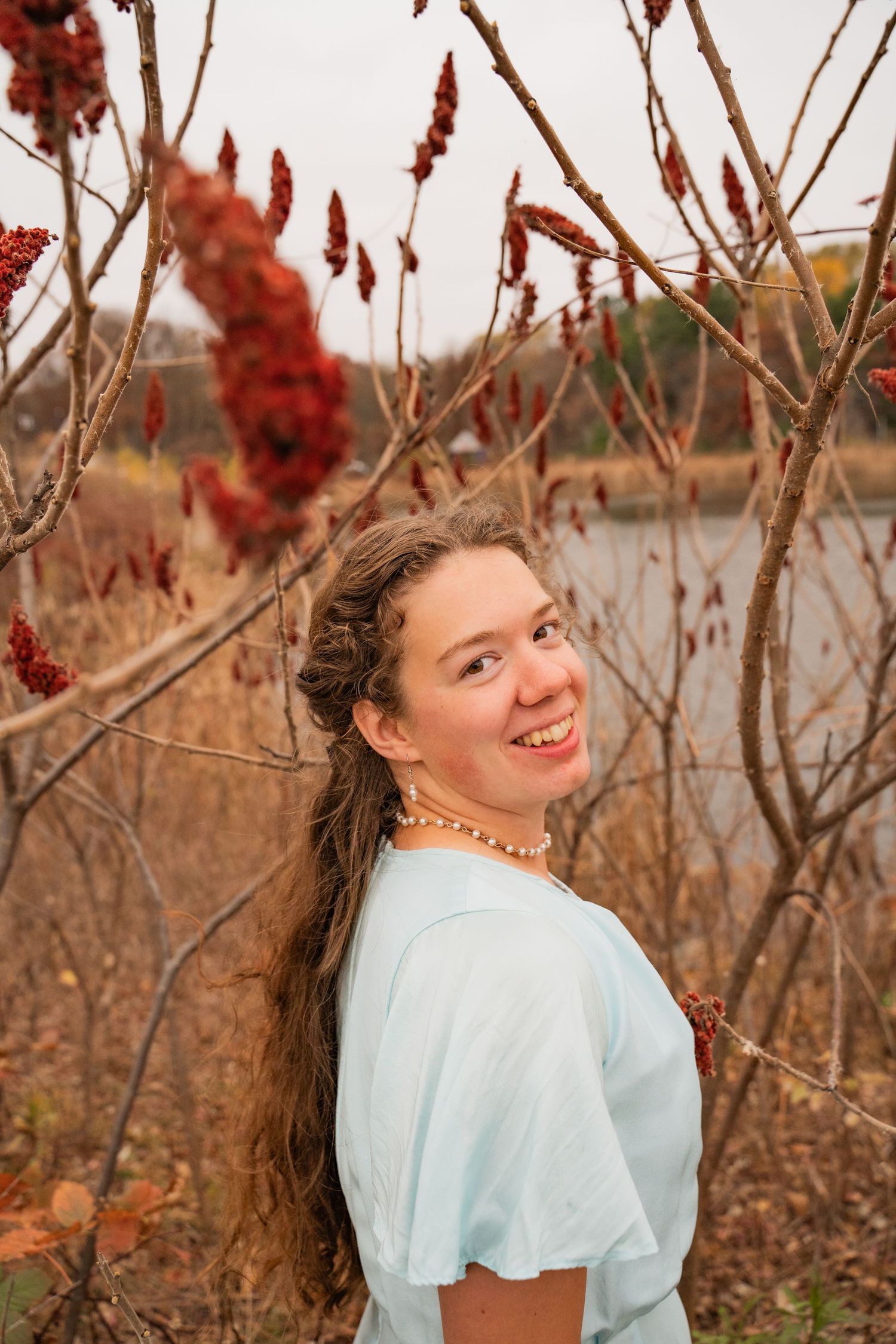 Whimsical outdoor portrait with light blue dress among red winter berries.