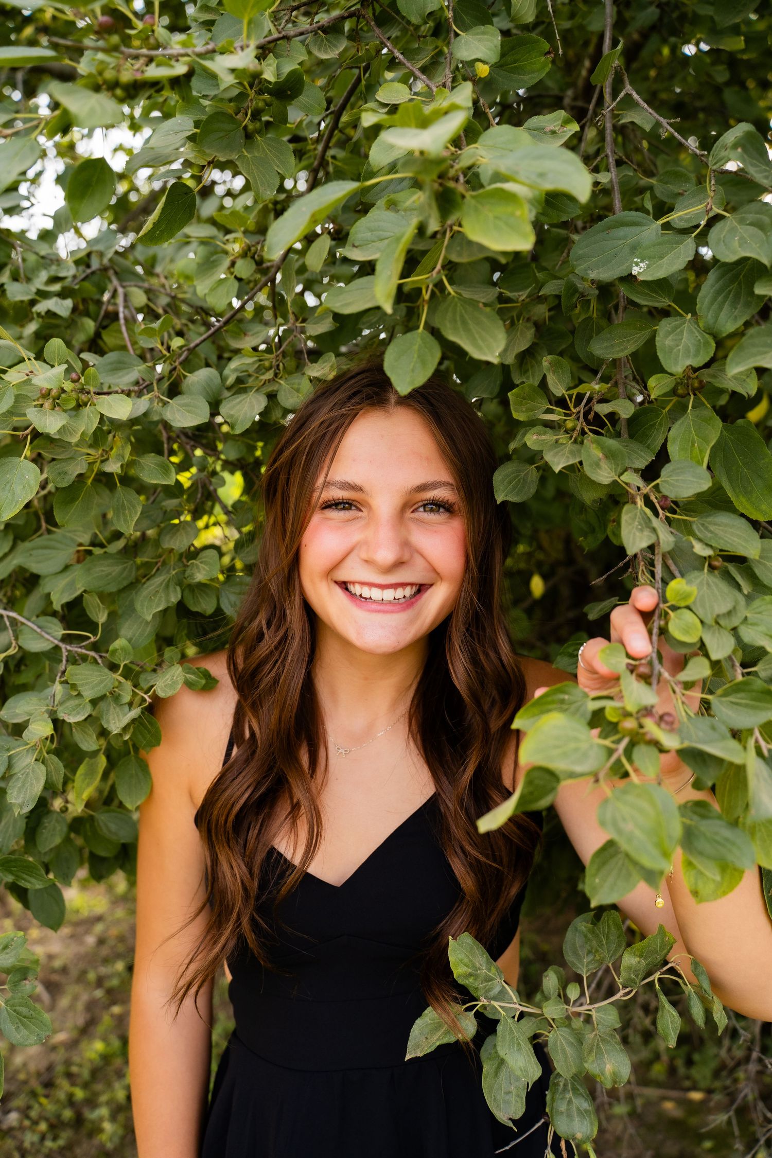 Natural portrait under green foliage with dappled sunlight creating a cheerful outdoor scene.