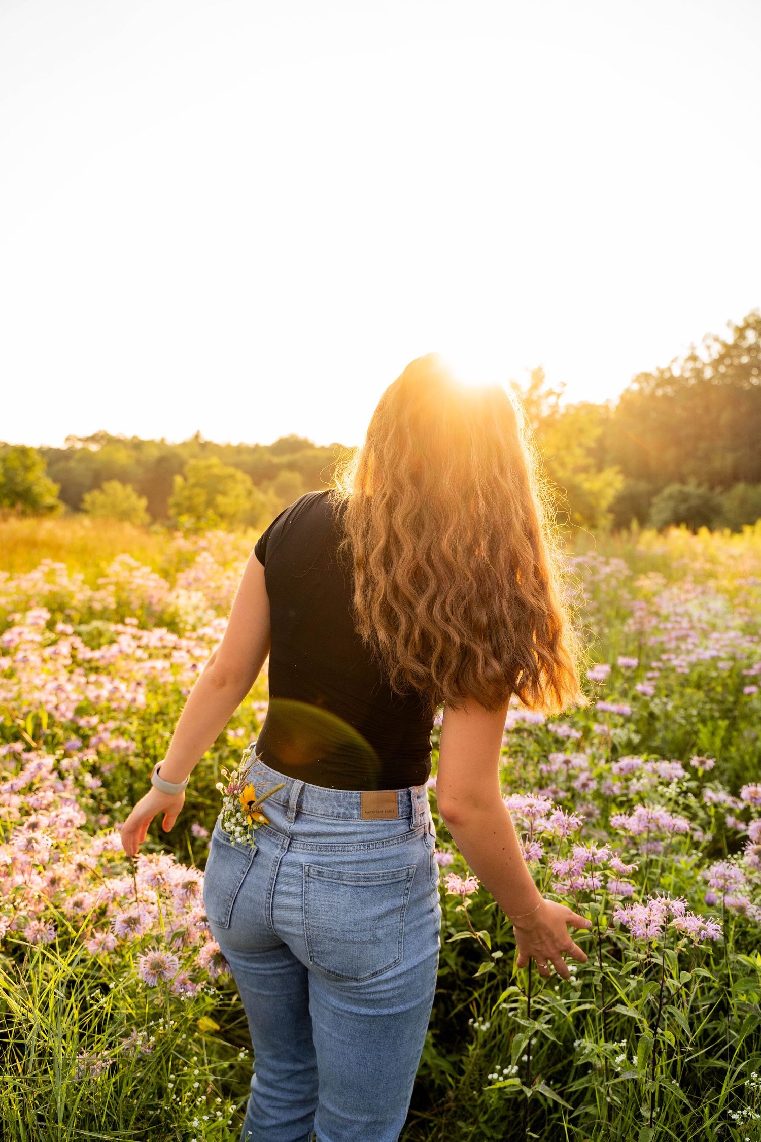 Person walking through wildflower field at sunset wearing jeans and black top.