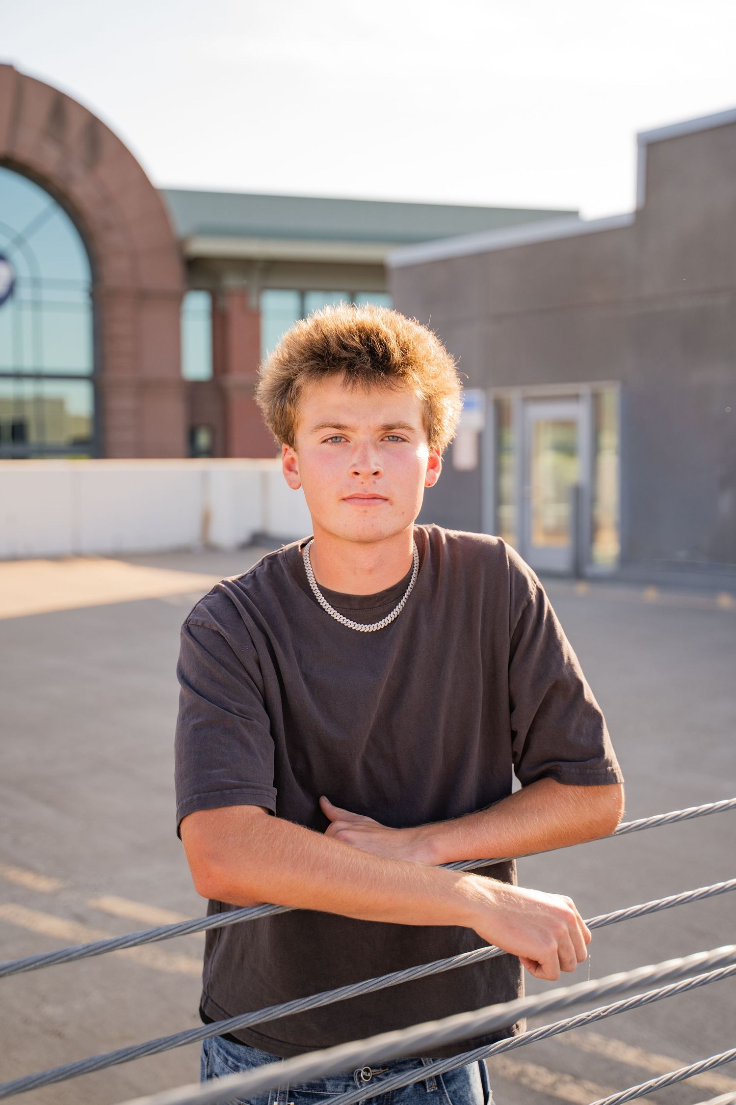Teen boy poses casually against metal railing in black t-shirt during an industrial style senior session outdoors.