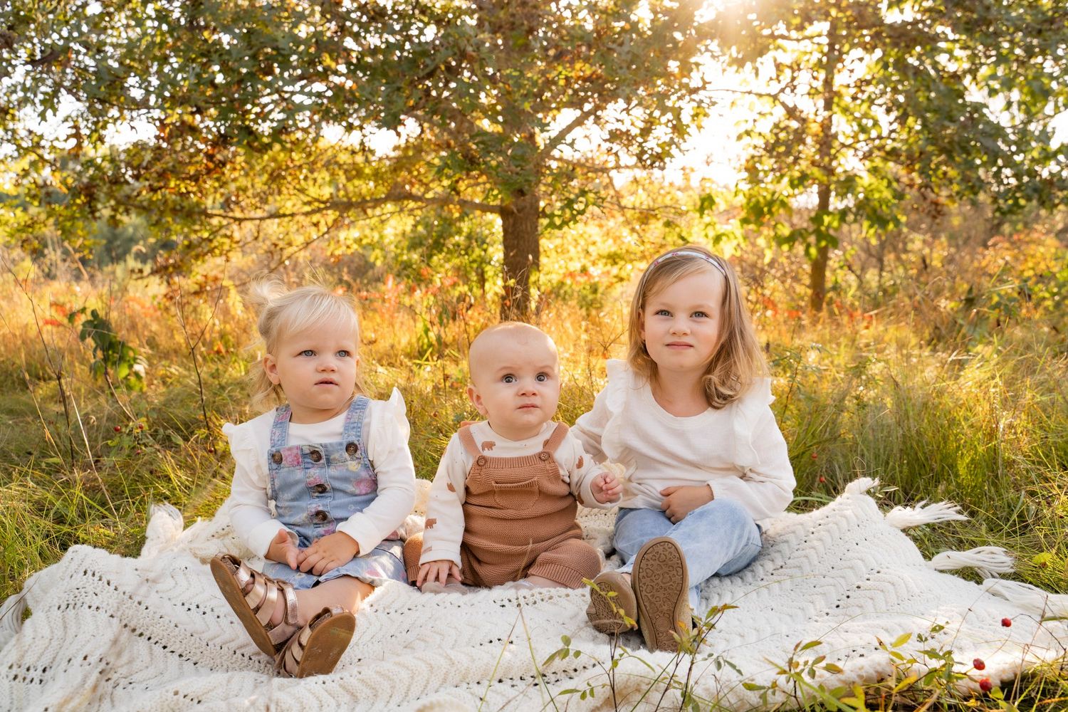 Extended family sitting together on white blanket during golden hour photo session.