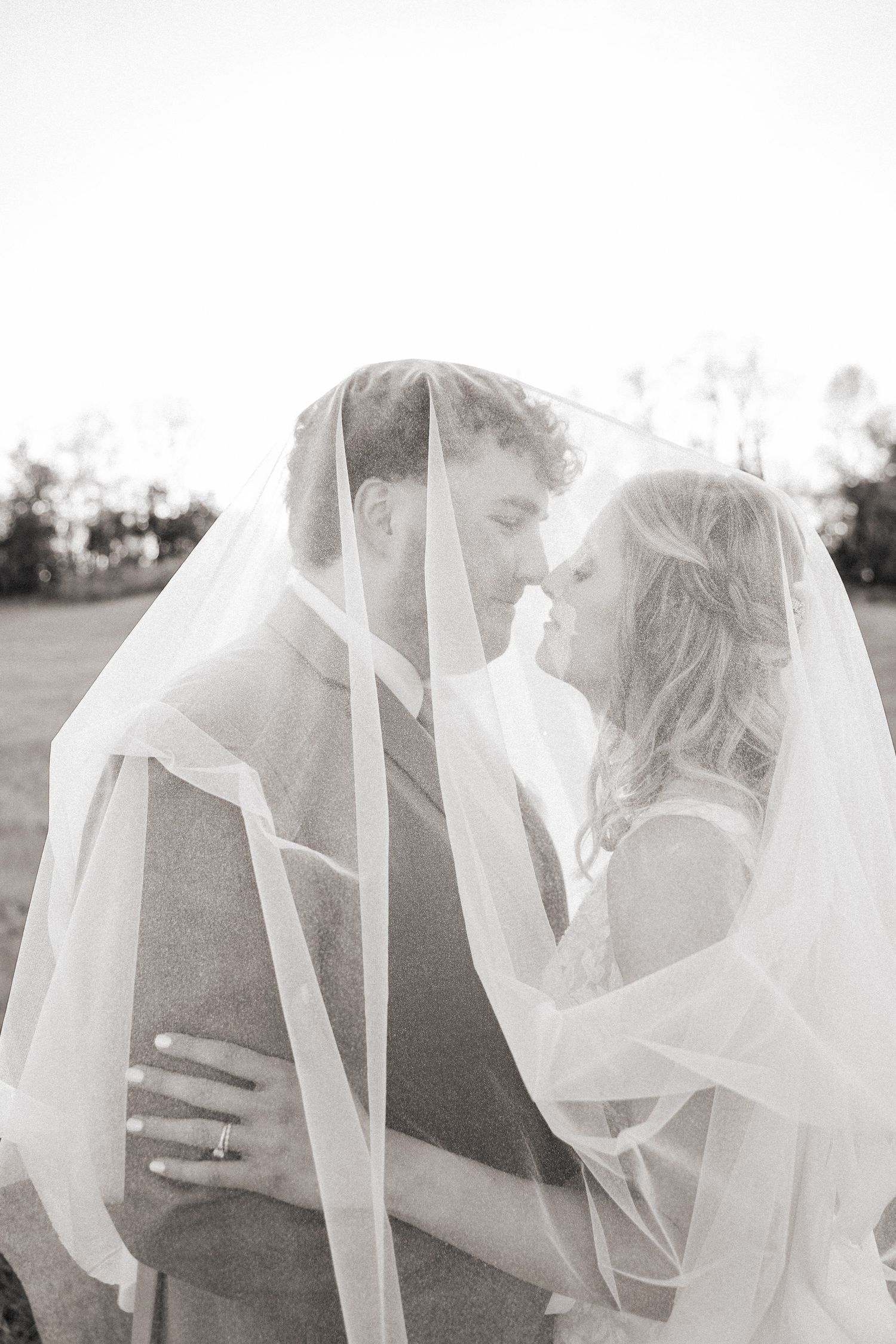 A romantic black and white wedding photo of a couple sharing an intimate moment under a flowing veil.
