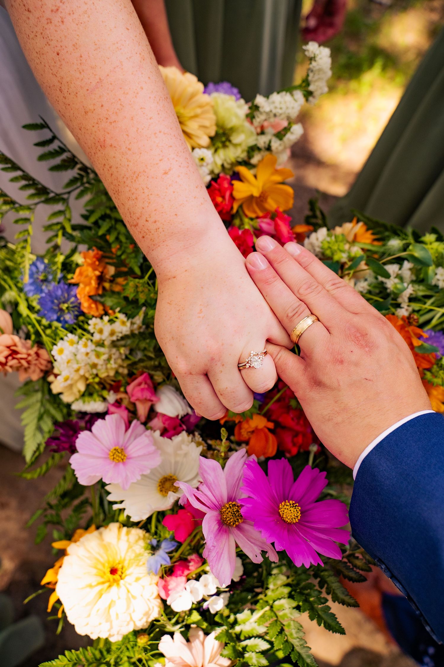 Close-up view of hands with wedding rings resting on a vibrant bouquet of colorful wildflowers and daisies in Wisconsin