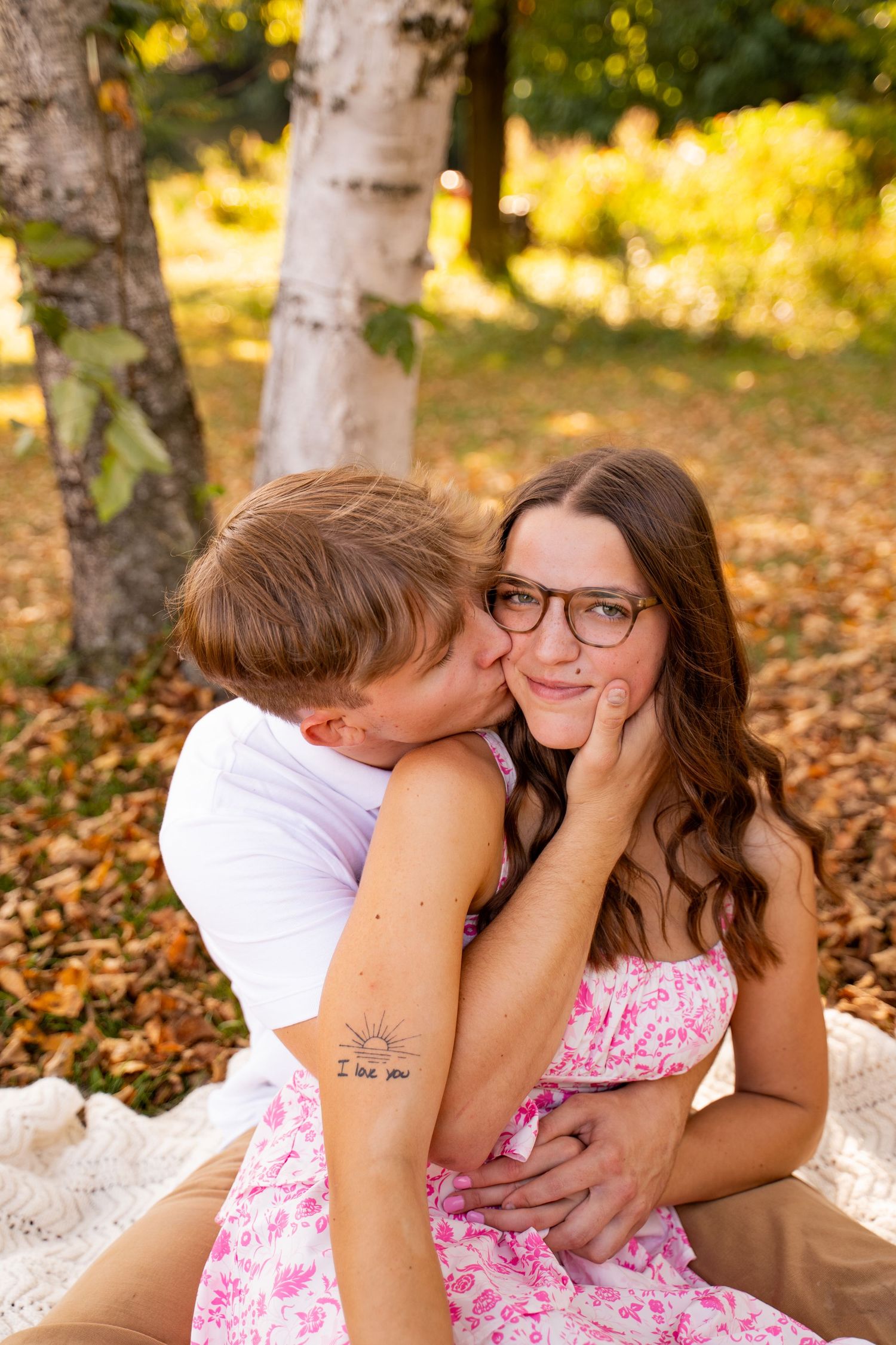 Sweet outdoor photoshoot in a wooded area with birch trees and fallen autumn leaves.