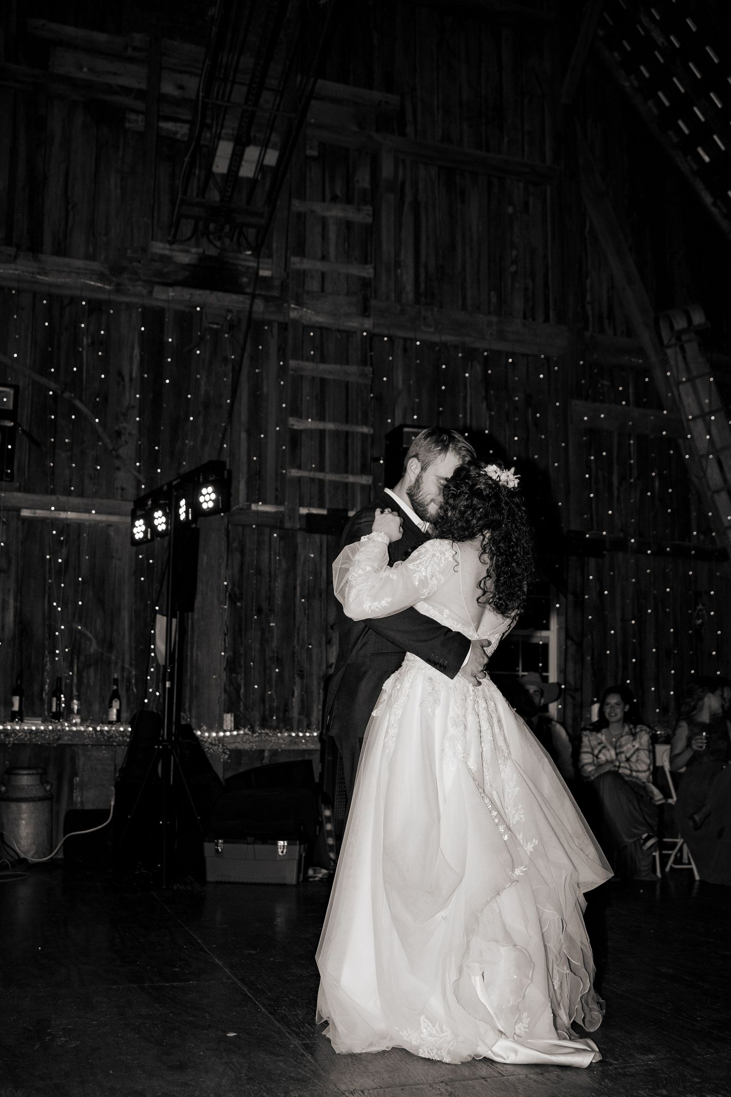 Black and white photo of a romantic dance in a barn with twinkling lights.