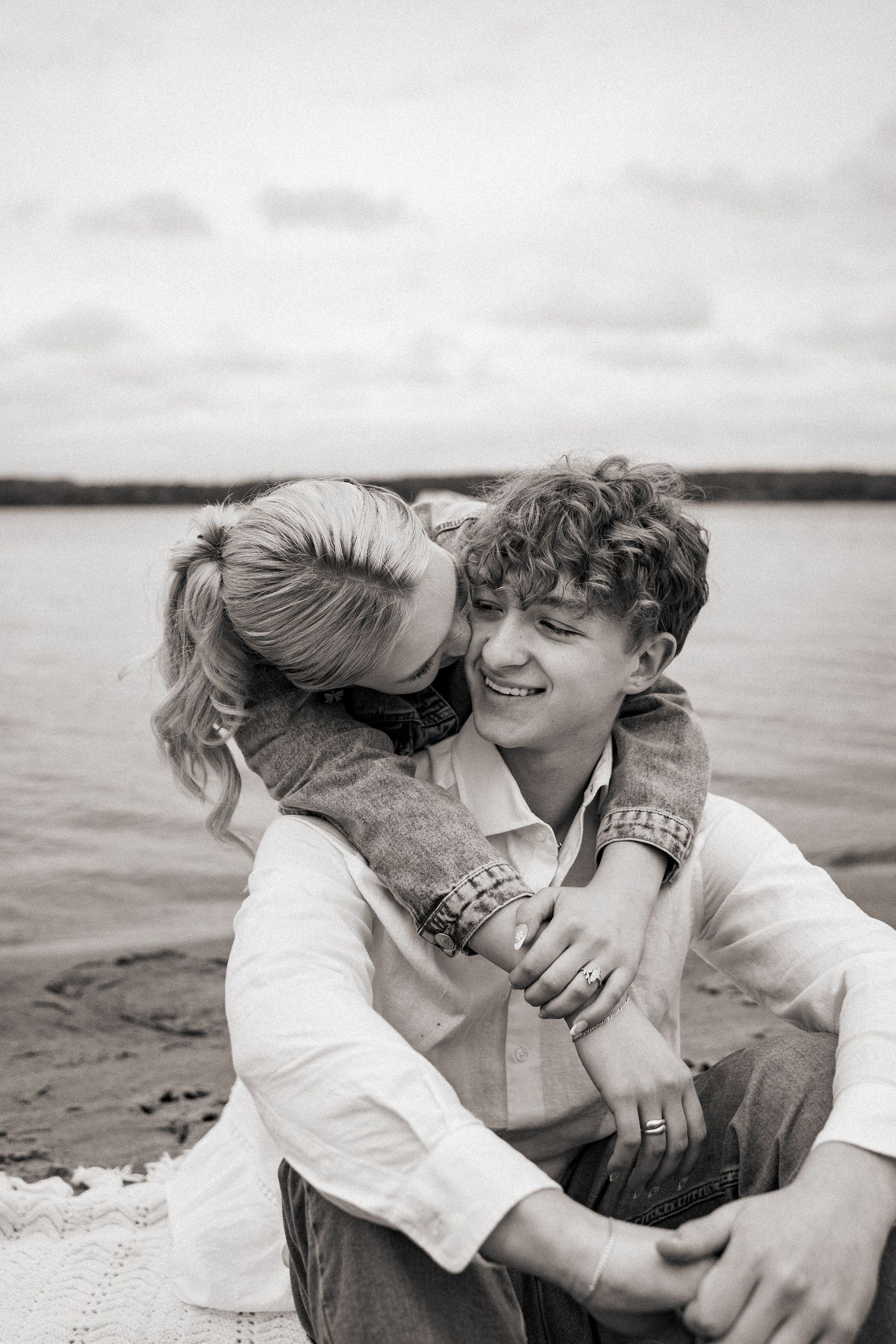 A playful black and white photo of a couple sharing an intimate moment on a beach.