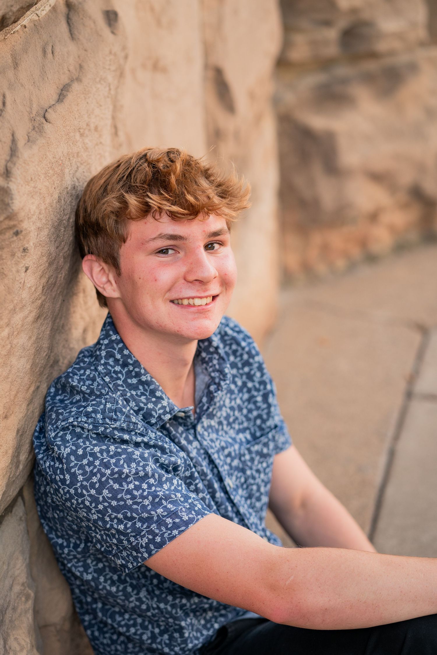 Casual portrait against stone wall showing joyful expression and blue patterned shirt.
