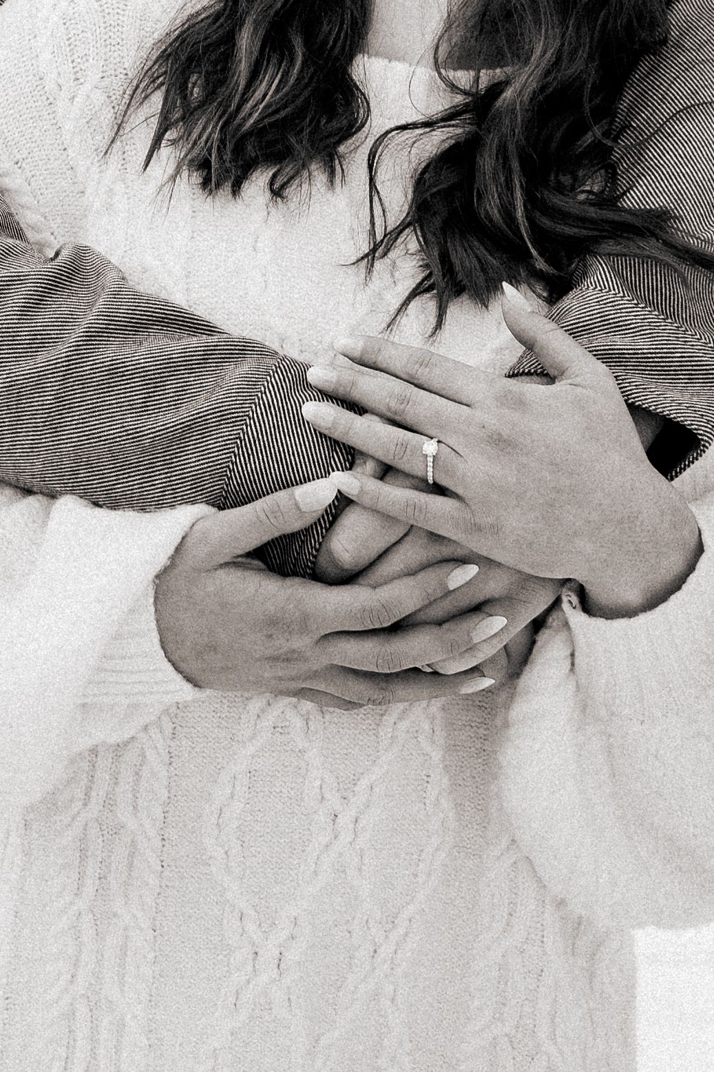 Close-up black and white photo of hands with rings in an intimate embrace.