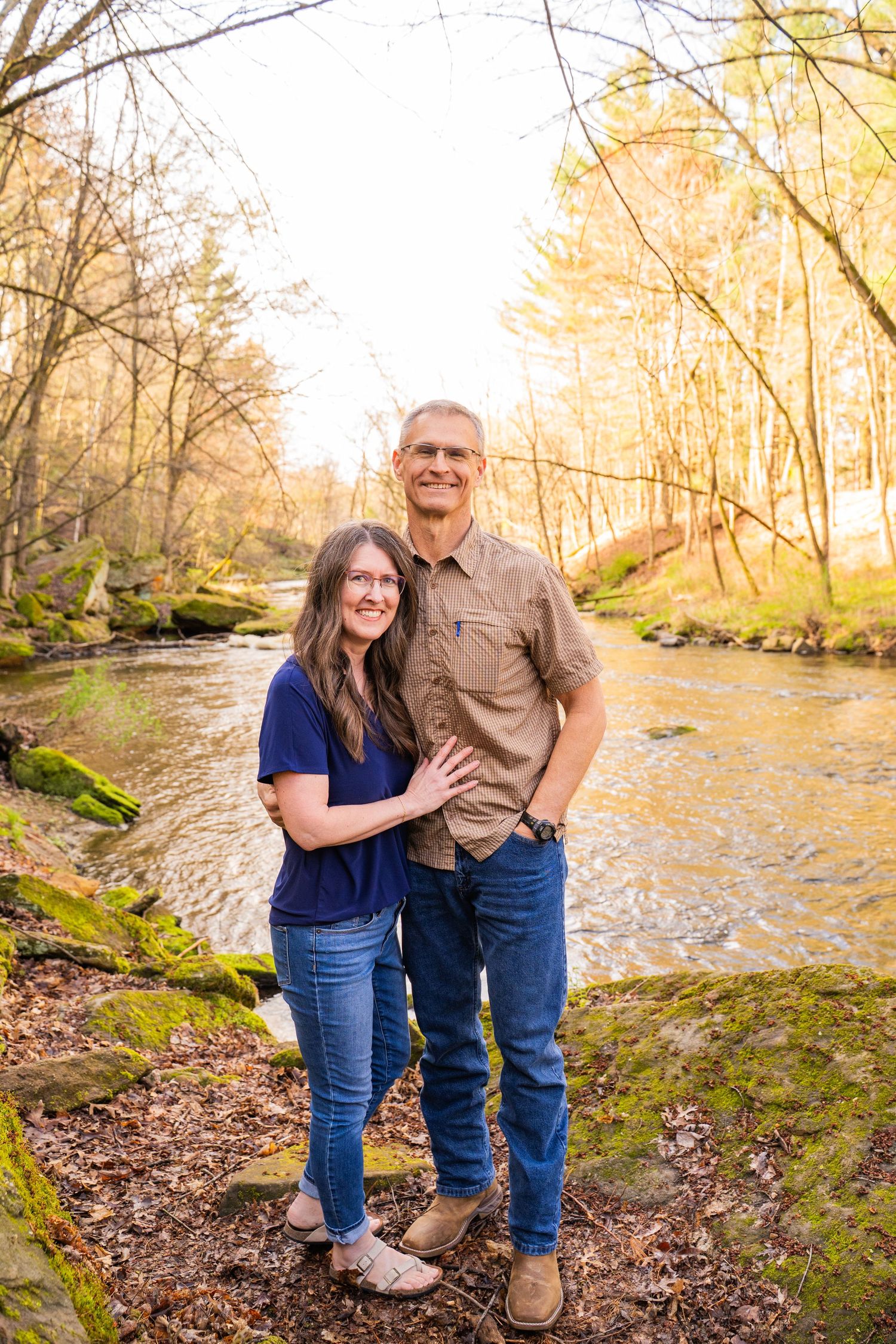 Couple embracing by creek in autumn forest during golden hour.
