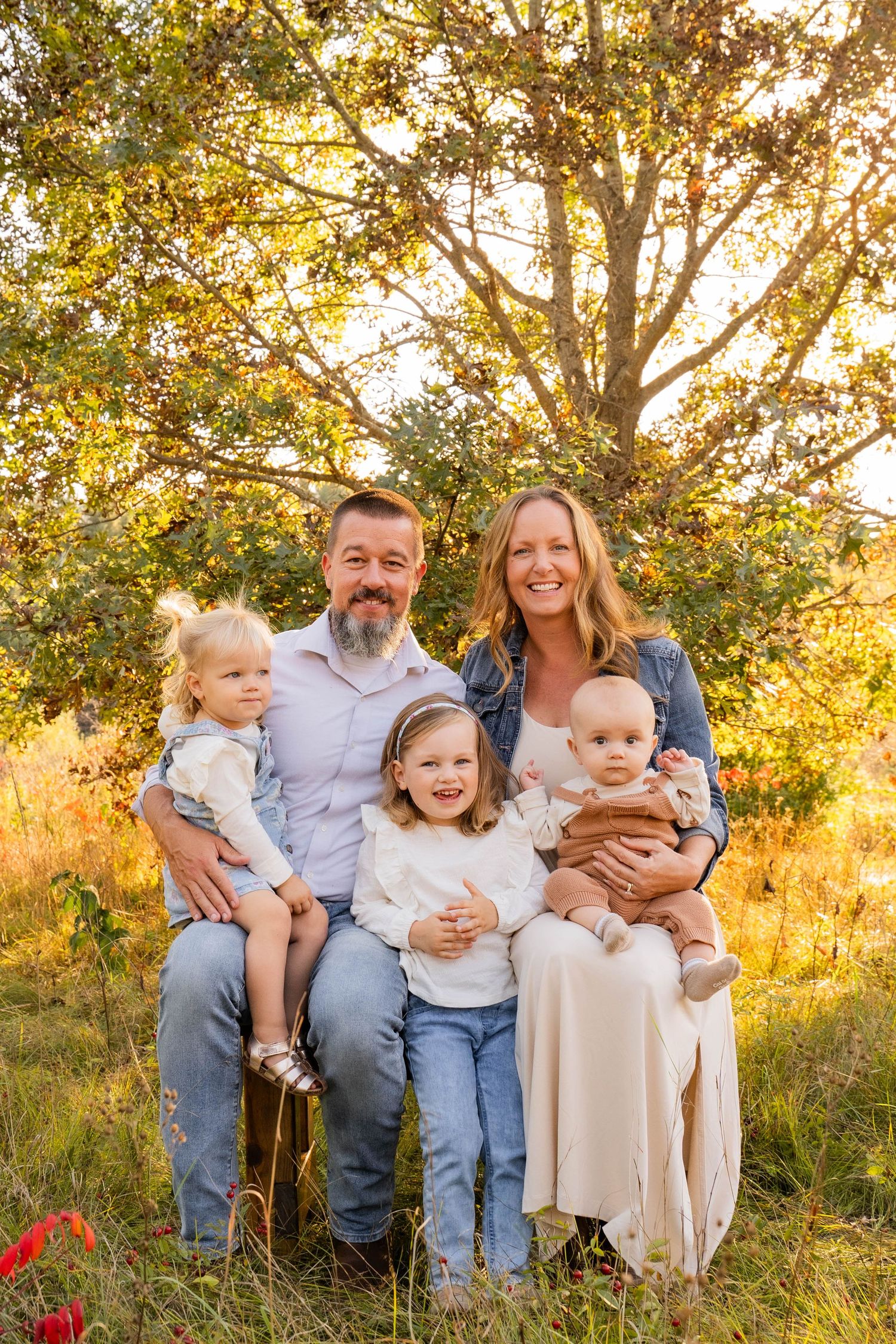 Family portrait outdoors with golden sunset light filtering through trees.