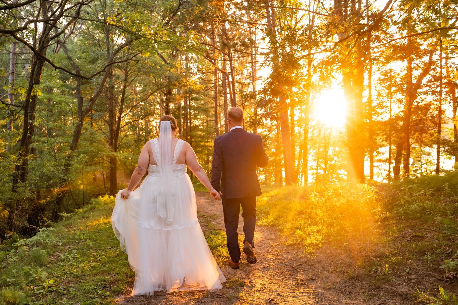 Silhouettes of a couple walking through a forest path at sunset with golden light streaming through trees.