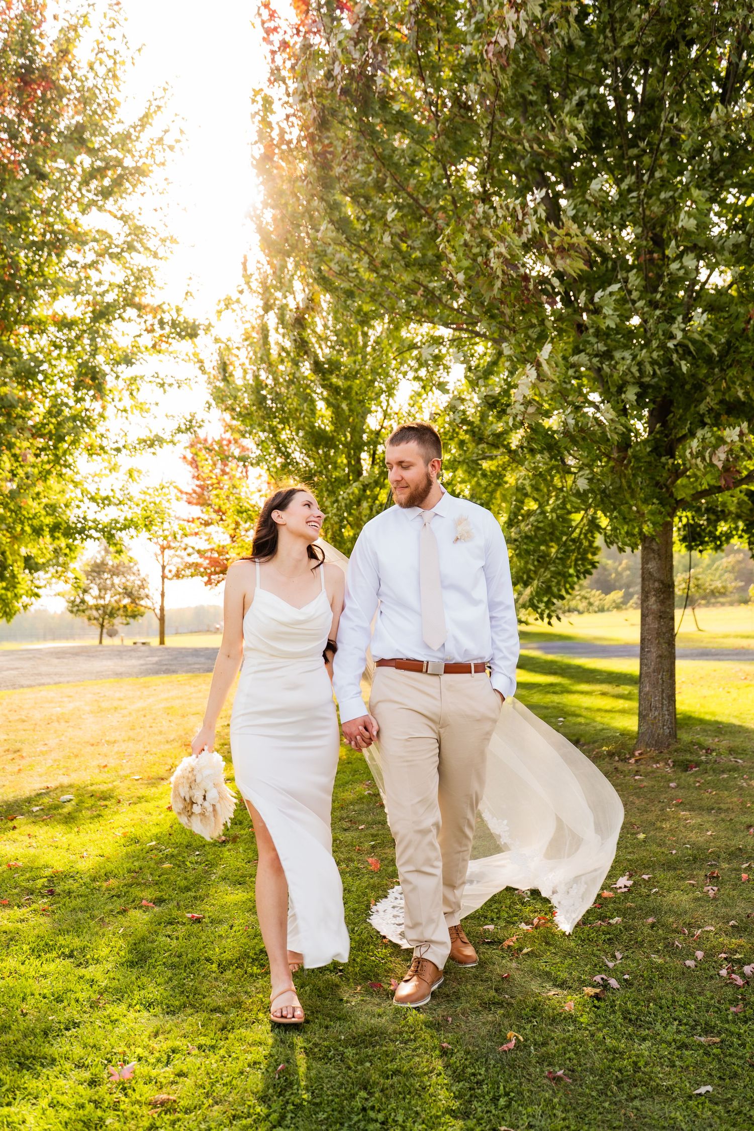 A wedding couple walks hand in hand at a intimate wedding with golden light filtering through the trees in Wisconsin