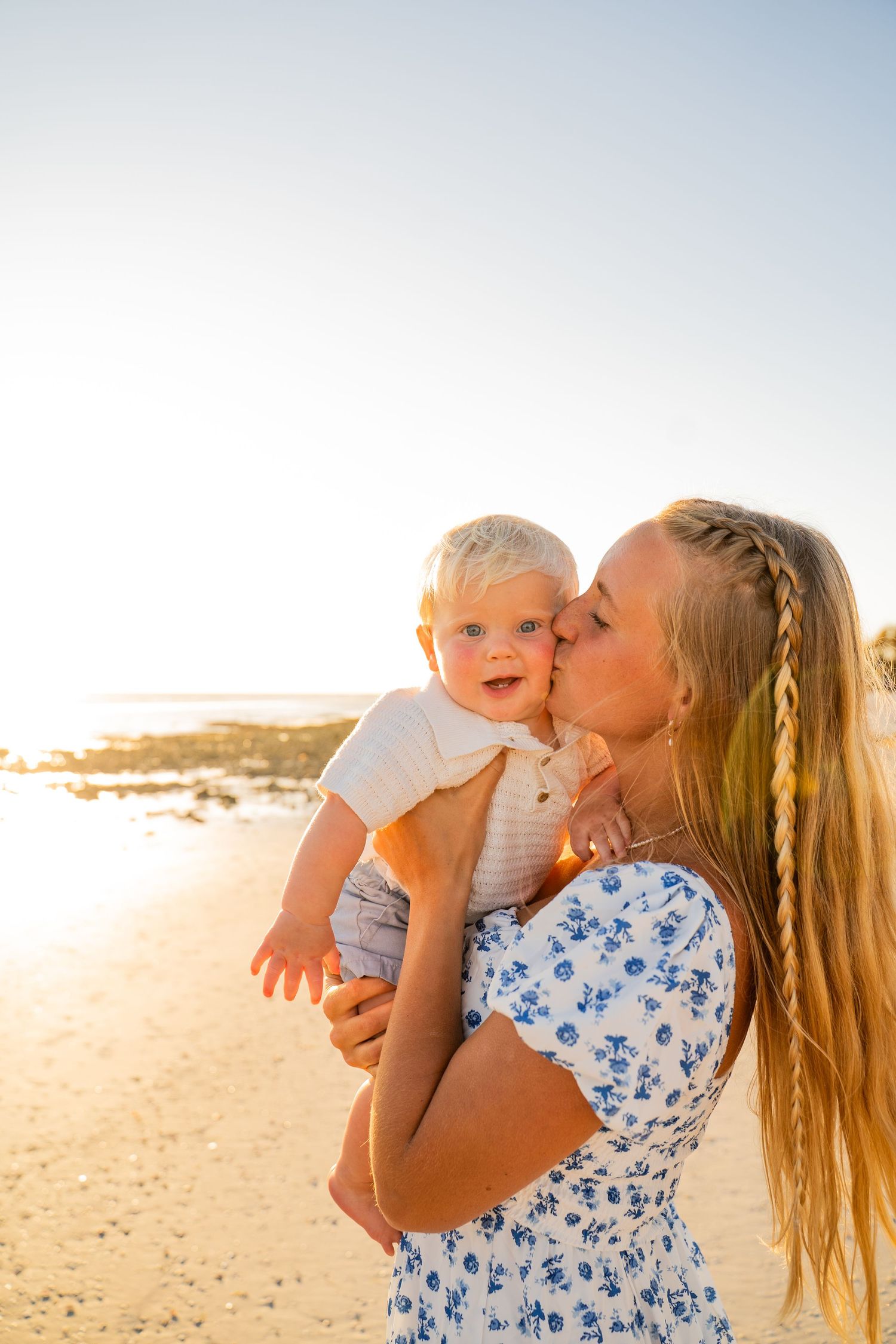 A heartwarming beach scene at sunset with a parent and baby sharing an intimate moment.
