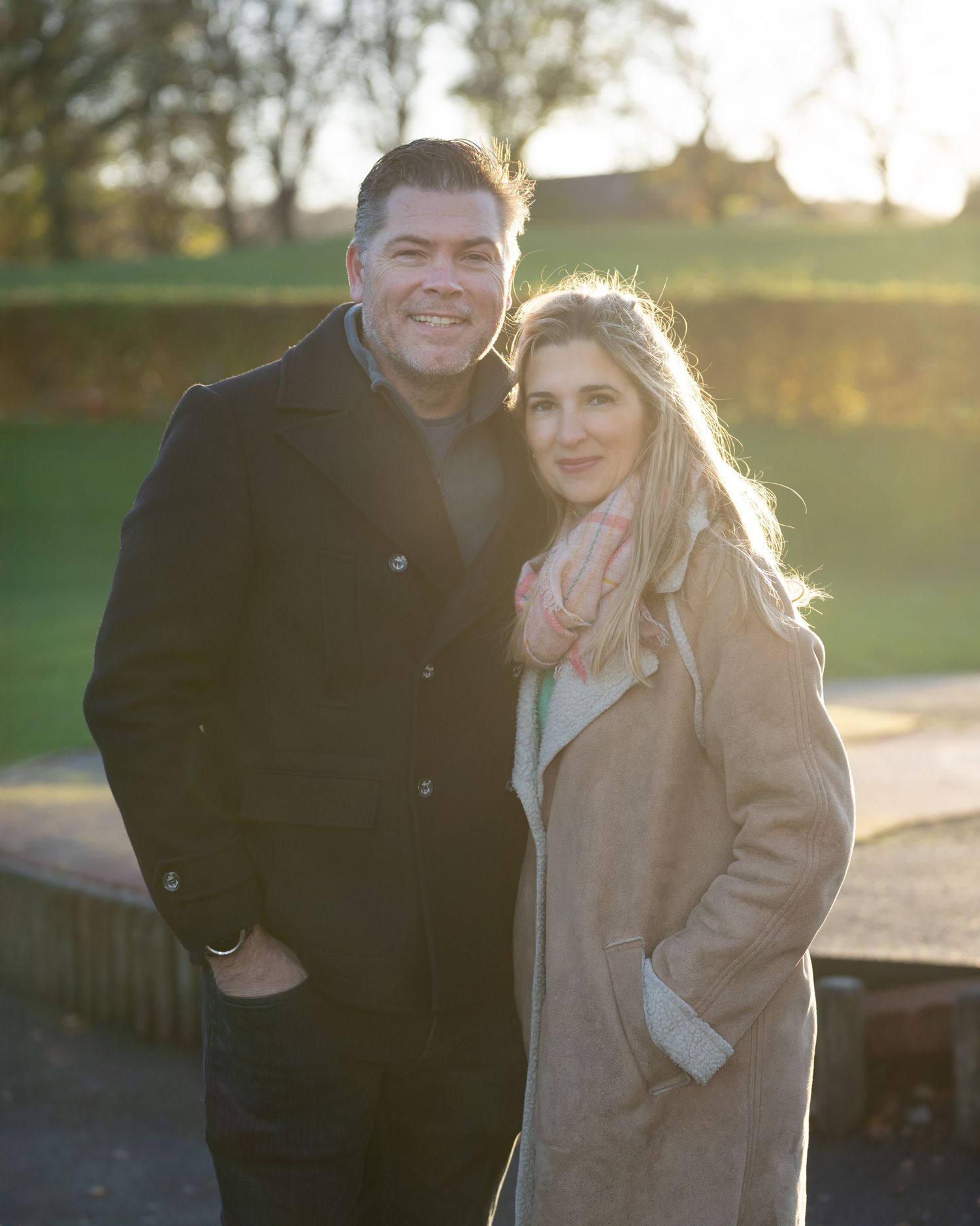 Family photograph. Couple in winter coats smiling at camera during golden hour.