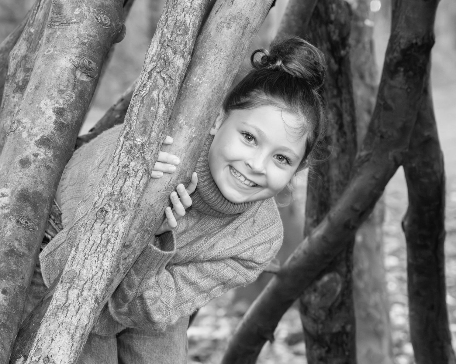 Family photograph. Black and white portrait of a child peeking through tree branches with a playful smile.