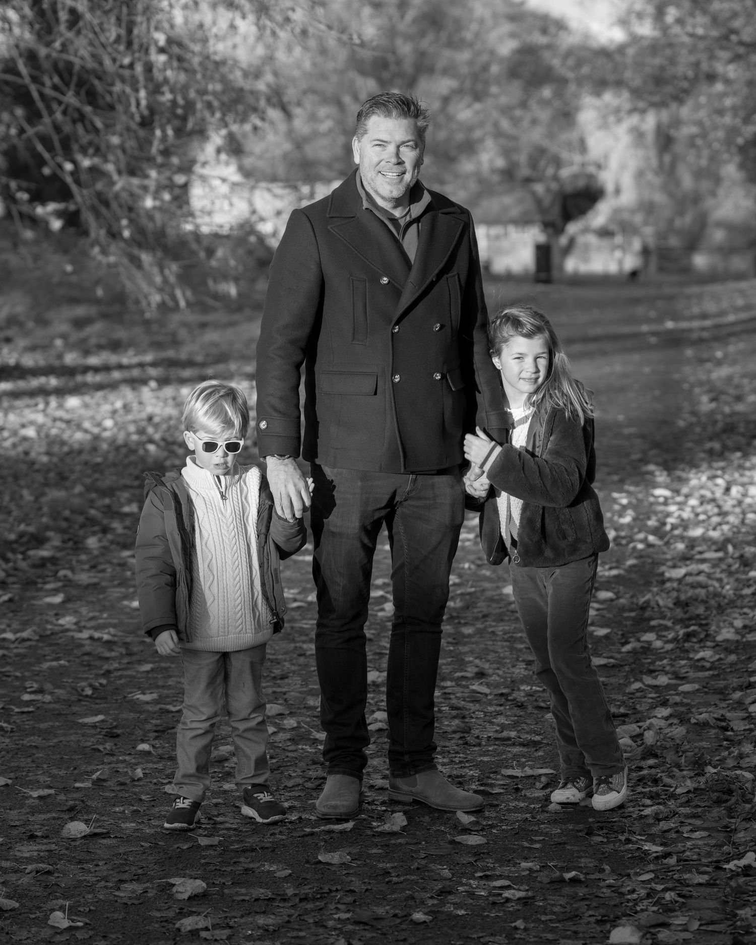 Family photograph. Black and white portrait of family in winter coats standing on a leaf-covered path.