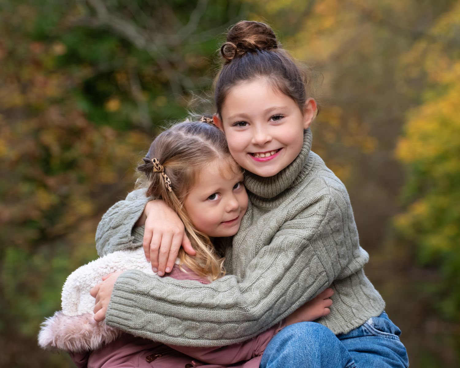 Two children in sweaters embrace while sitting outdoors during autumn.