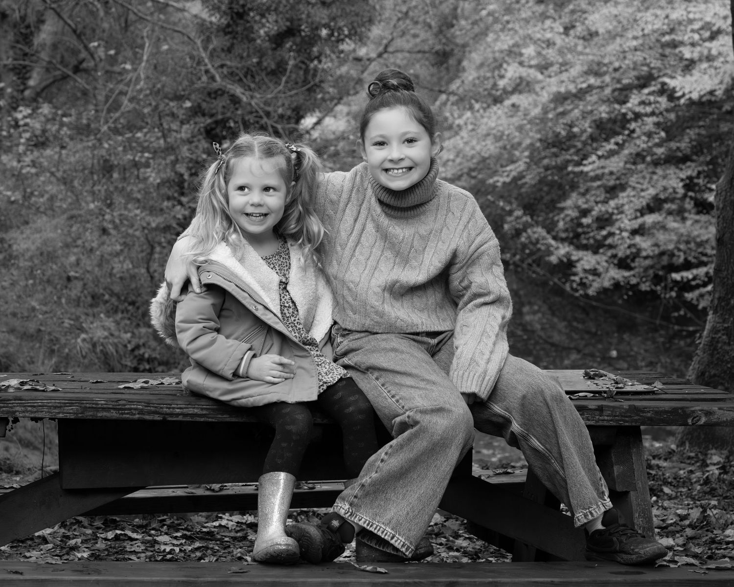 Family photograph. Children playing and laughing together on log in black and white nature setting.
