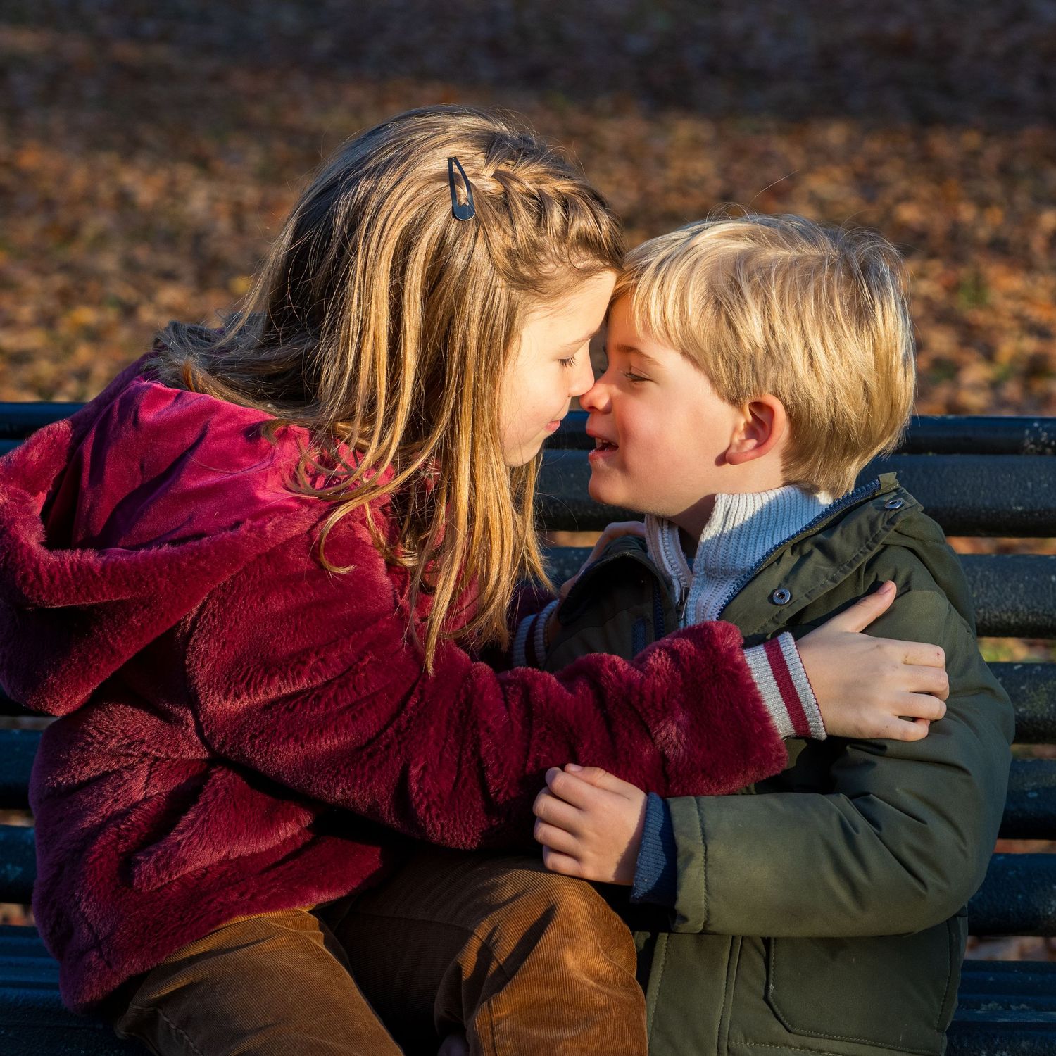 Family photograph. Two children sharing a sweet moment on a park bench in autumn.