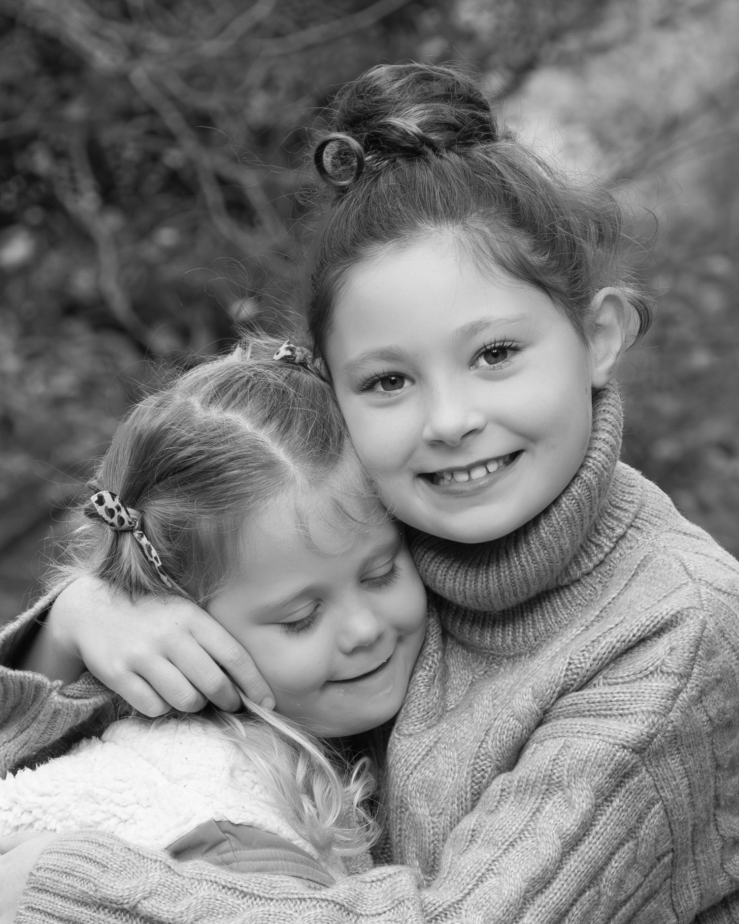 A heartwarming black and white portrait of two children sharing an affectionate embrace while wearing cozy sweaters.