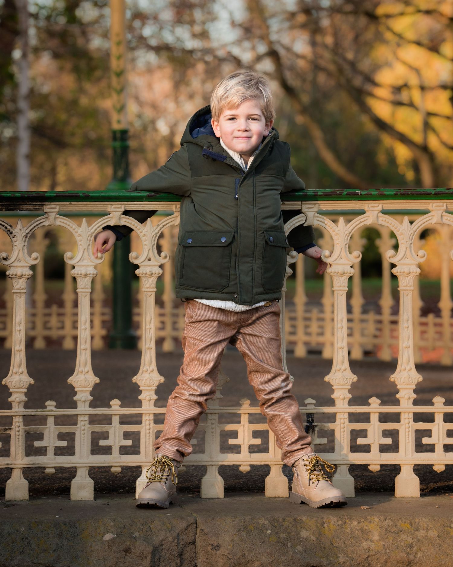 Family photograph. Child in winter coat standing on ornate railing during autumn.