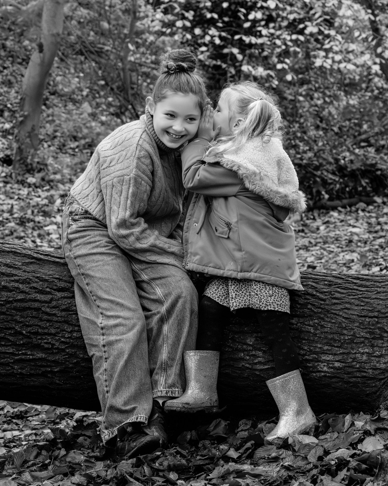 Family photograph. Children sitting together on fallen log in black and white outdoor photograph.