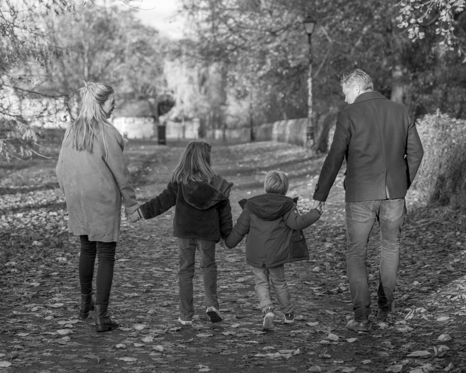 Family photograph. Family walking hand in hand along autumn path from behind.