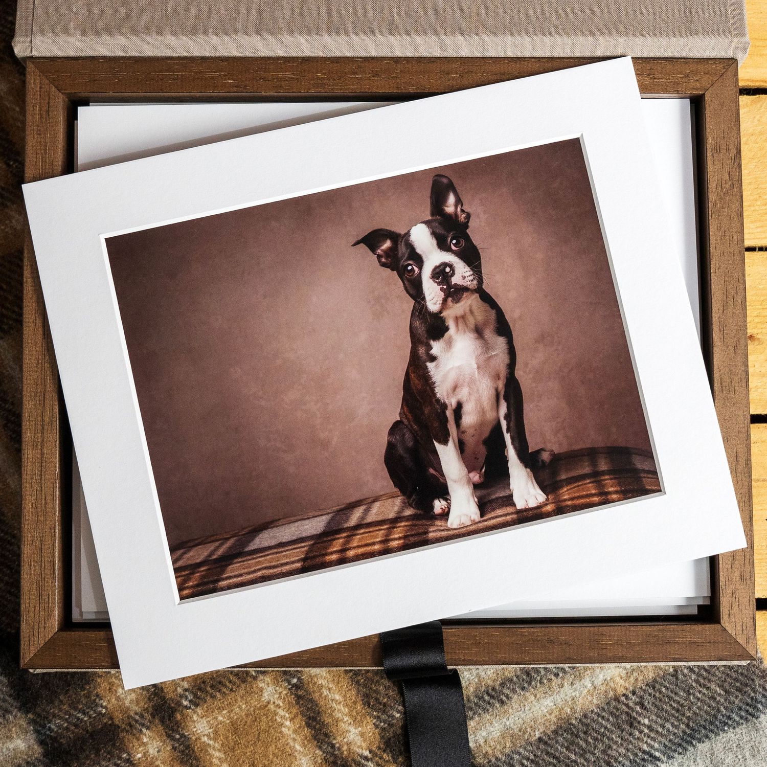 A matted portrait print of a Boston Terrier dog sitting on a plaid surface, displayed in a wooden keepsake box.