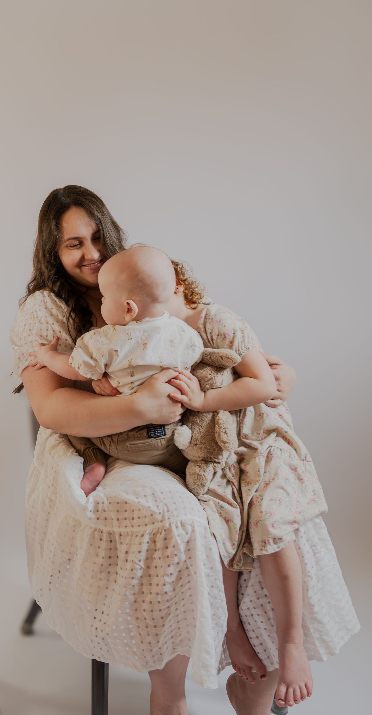 Intimate portrait of parent in white dress holding baby in matching outfit.