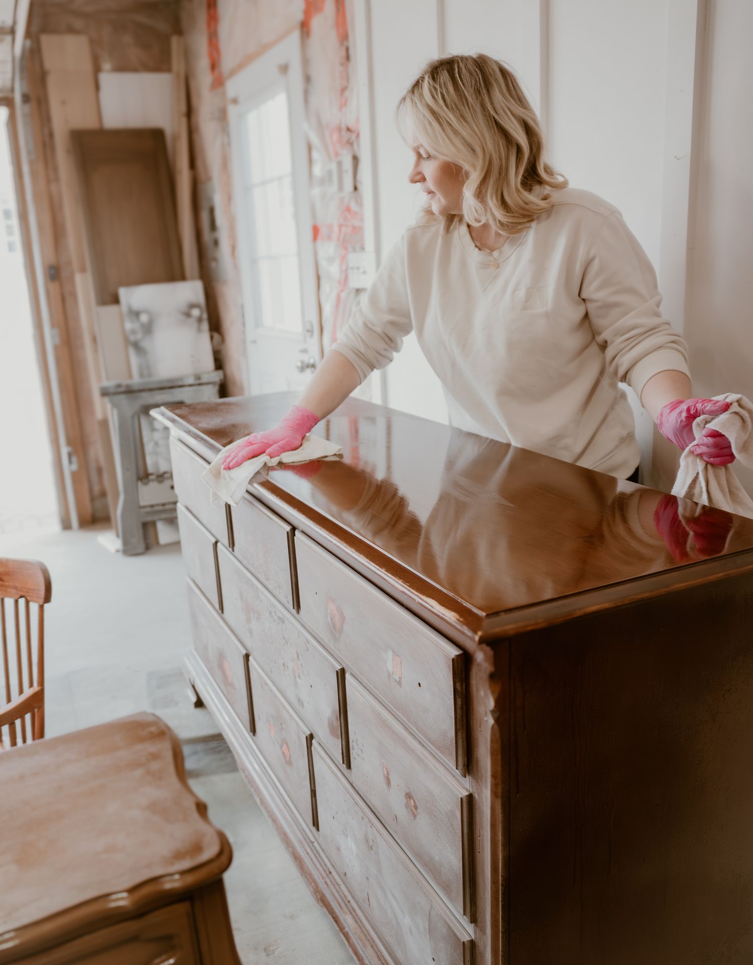 Person in cream sweater cleaning or organizing wooden dresser in room under renovation.