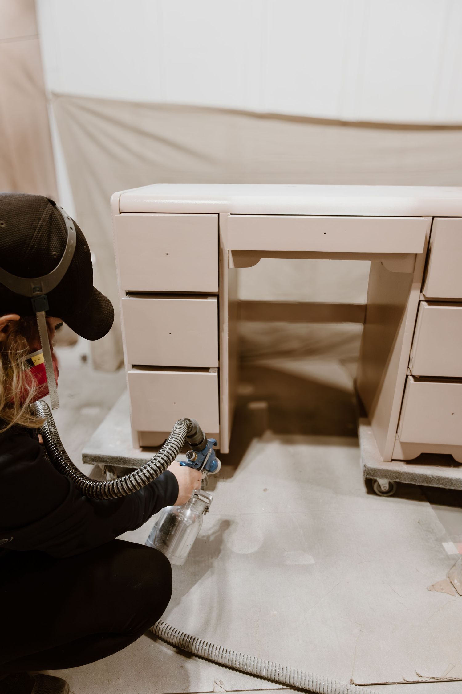 Person spray painting white desk with professional equipment in workshop setting.