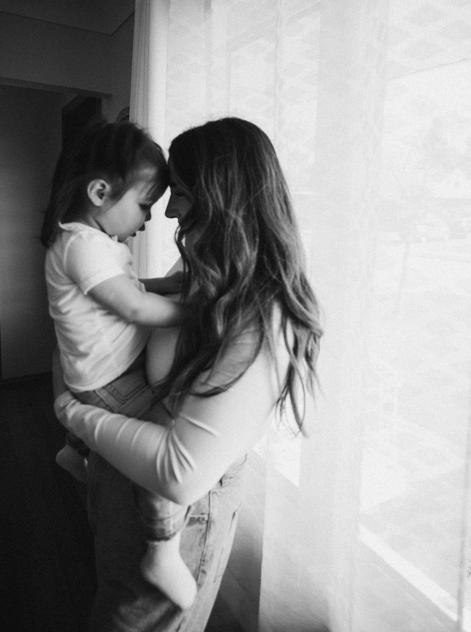 Black and white portrait of intimate parent-child moment by window.