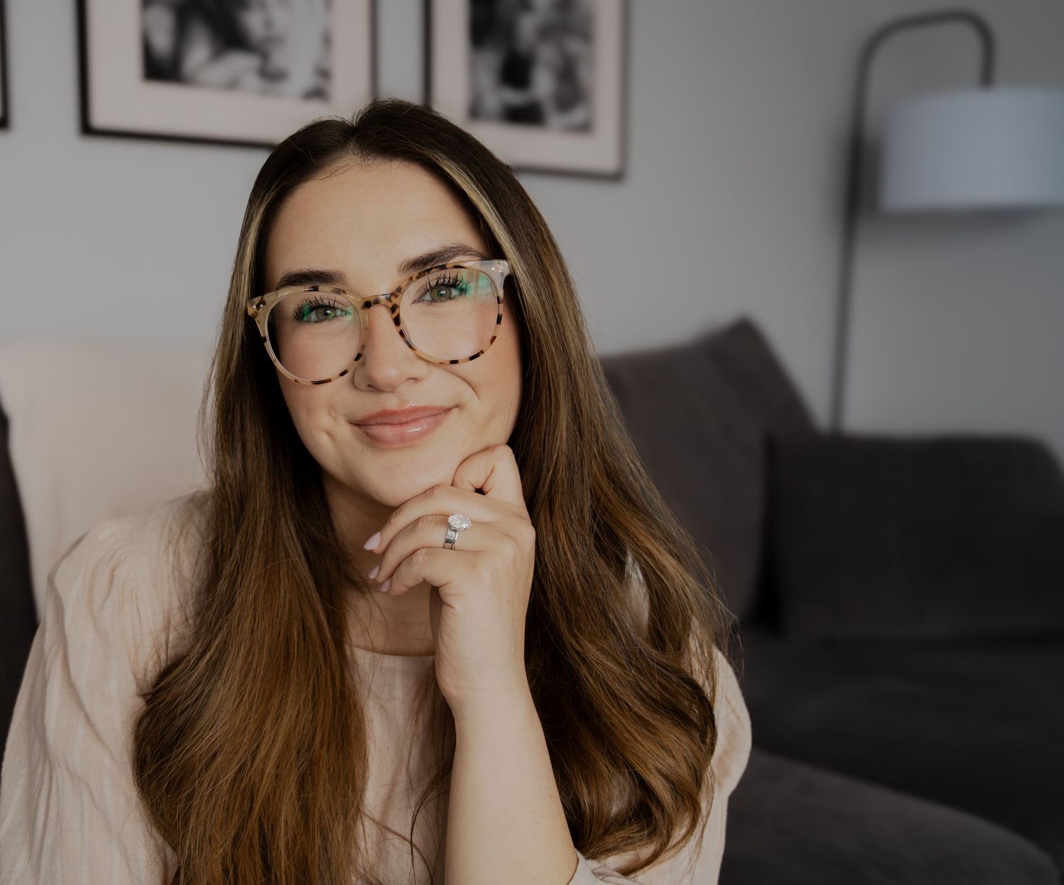 Lifestyle portrait of woman with glasses relaxing on grey couch with framed art in background.