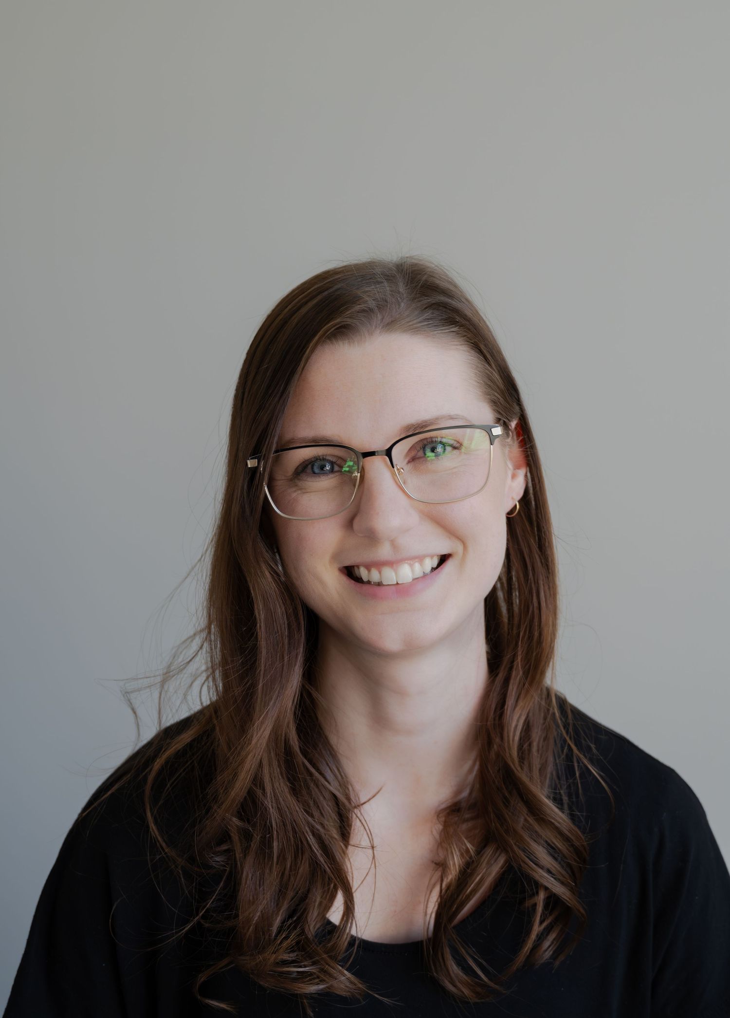 Professional headshot of person wearing glasses with natural lighting against gray background.