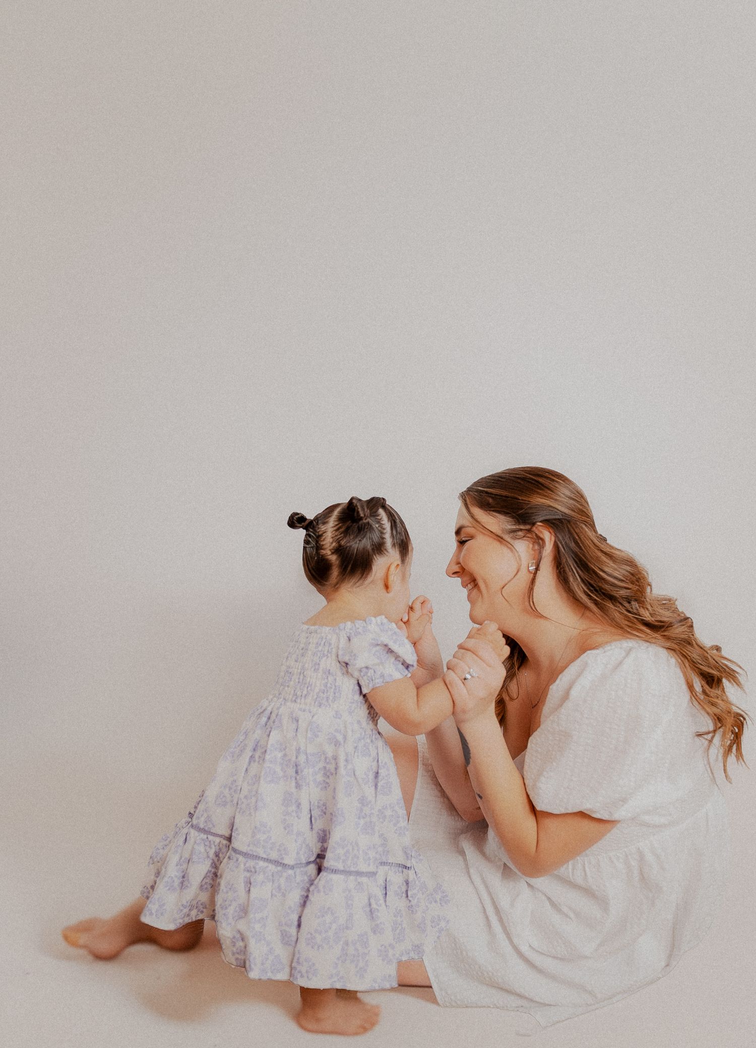 A joyful moment shared between two people wearing white dresses against a light grey background.