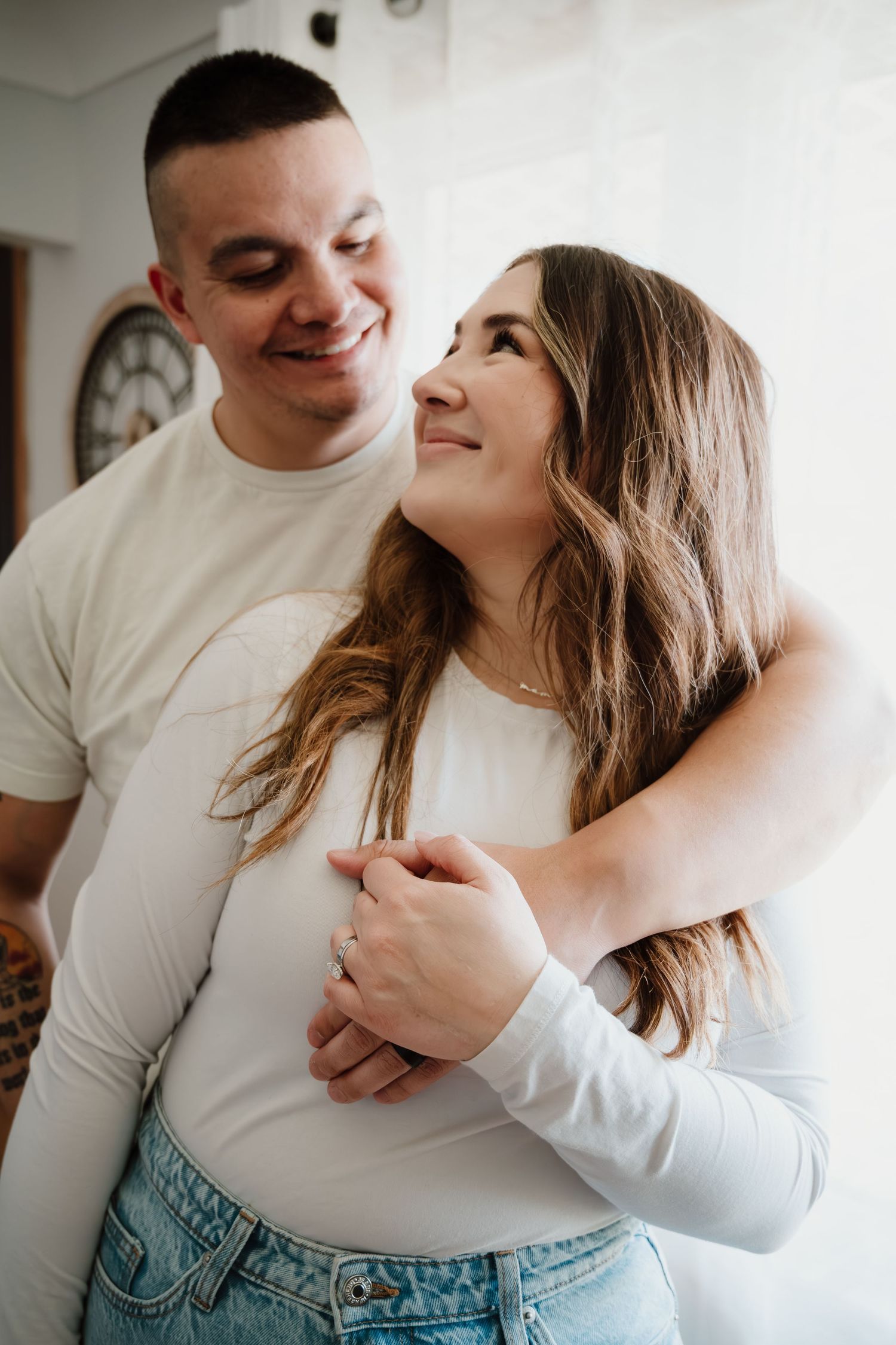 Intimate couple portrait with white shirts embracing against white wall.