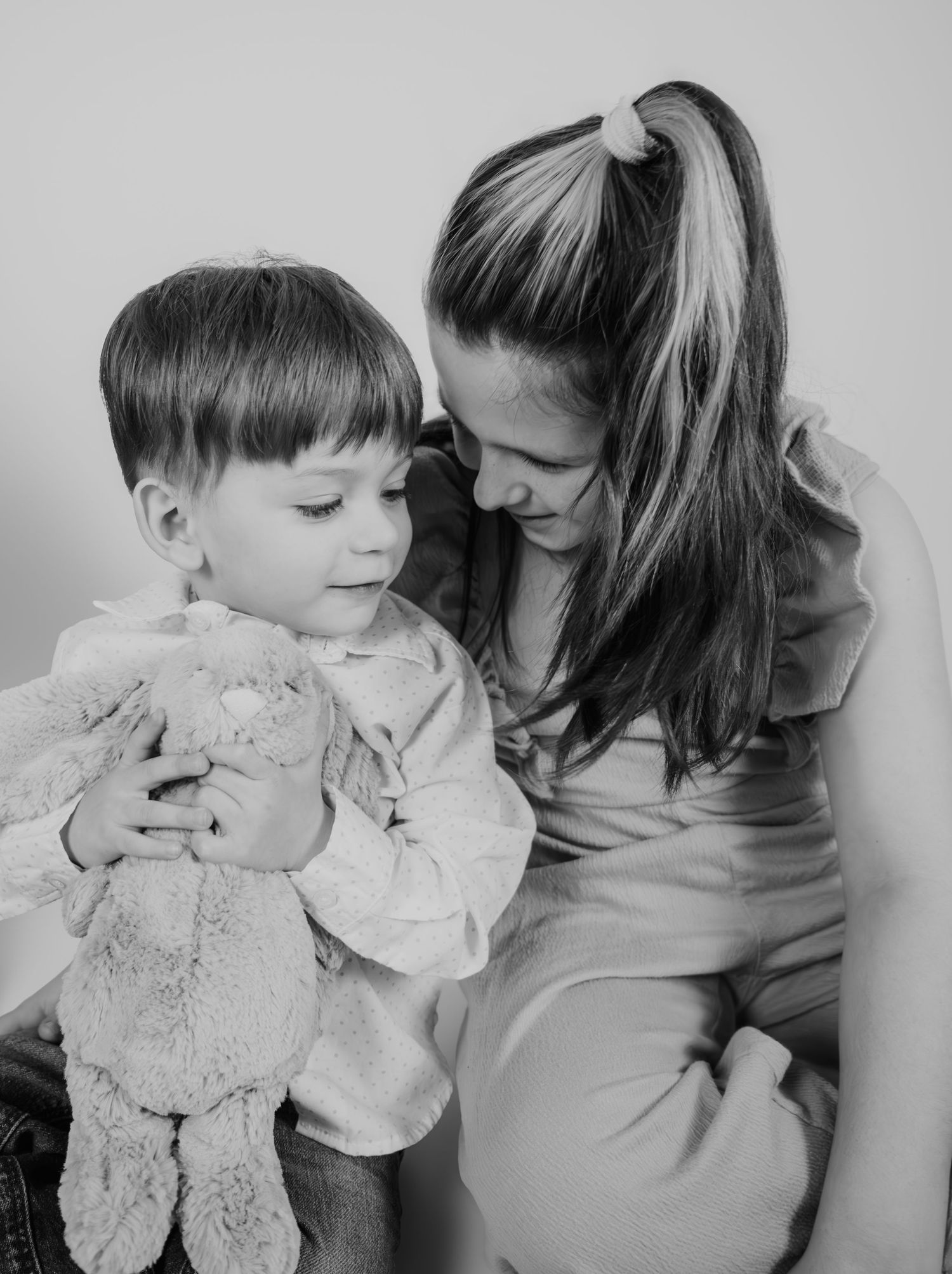 Parent and child sharing tender moment while holding plush toy in monochrome setting.
