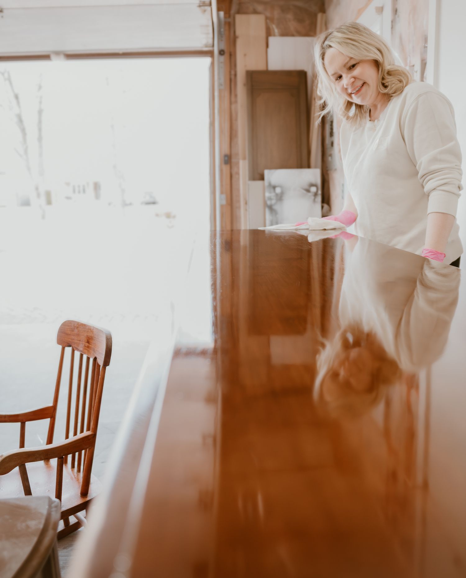 Person in white sweater working on furniture restoration project in bright space.