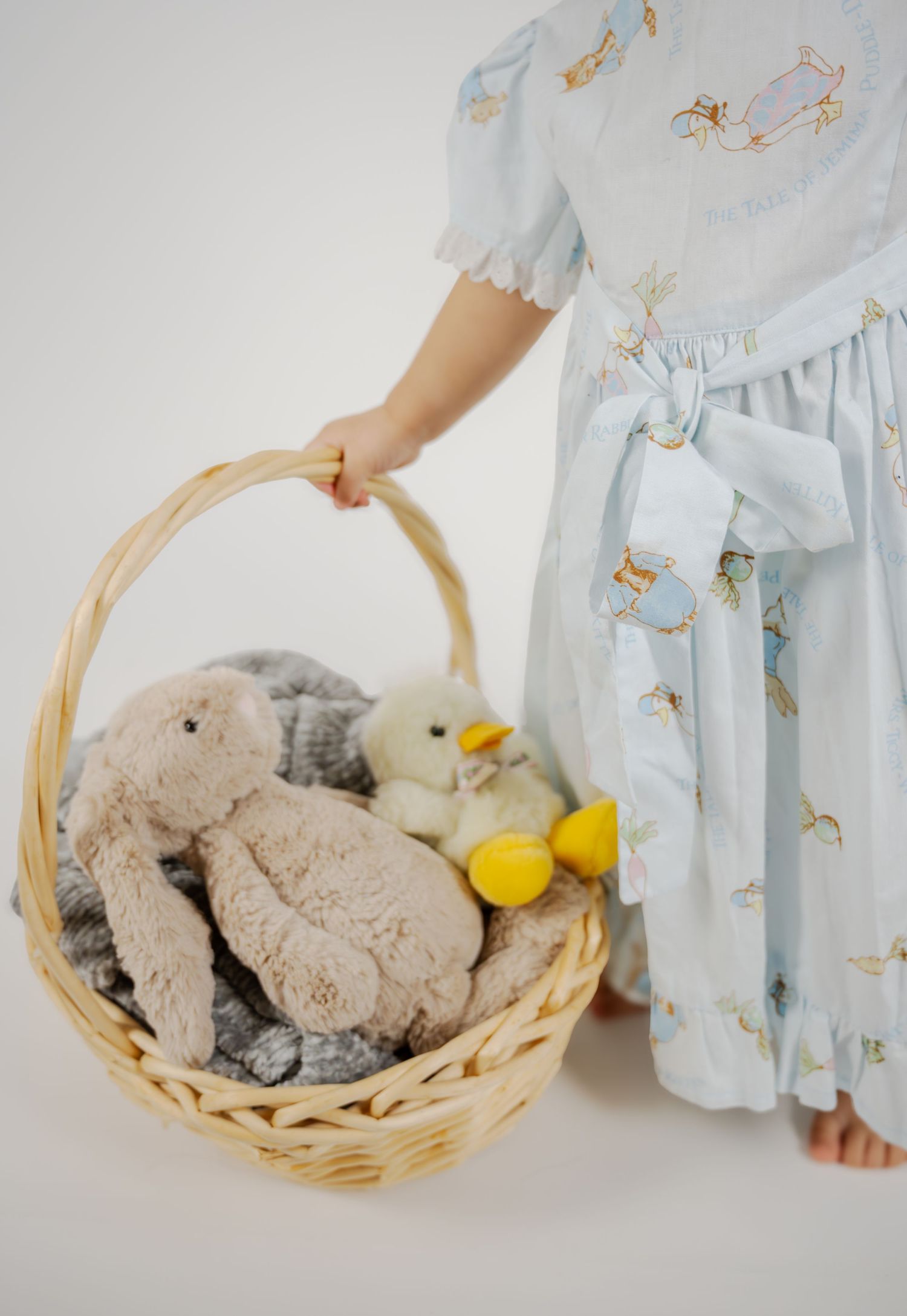 A woven basket filled with plush toys and a blue patterned dress visible in the frame.