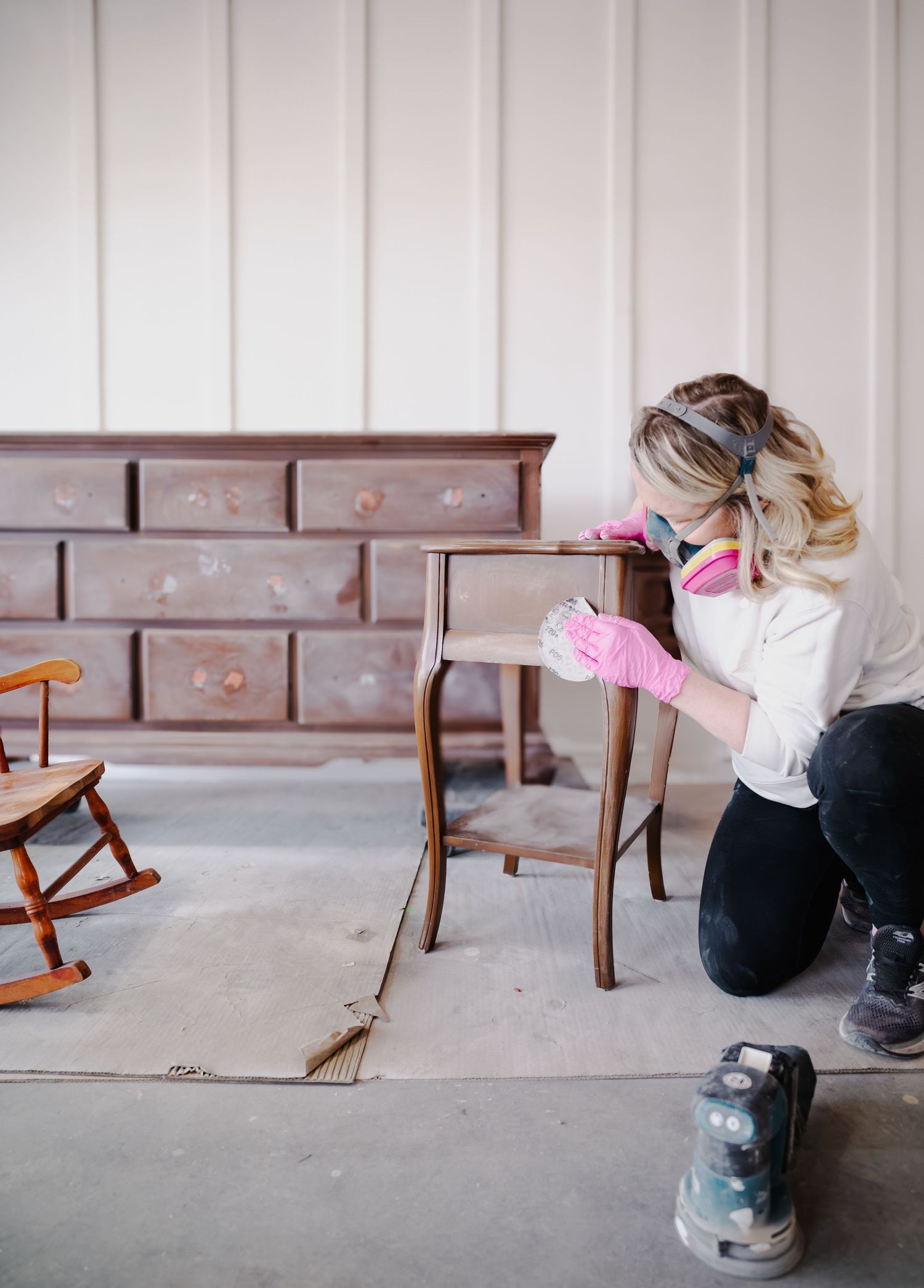 Person in protective gear refinishing wooden furniture on workshop floor.