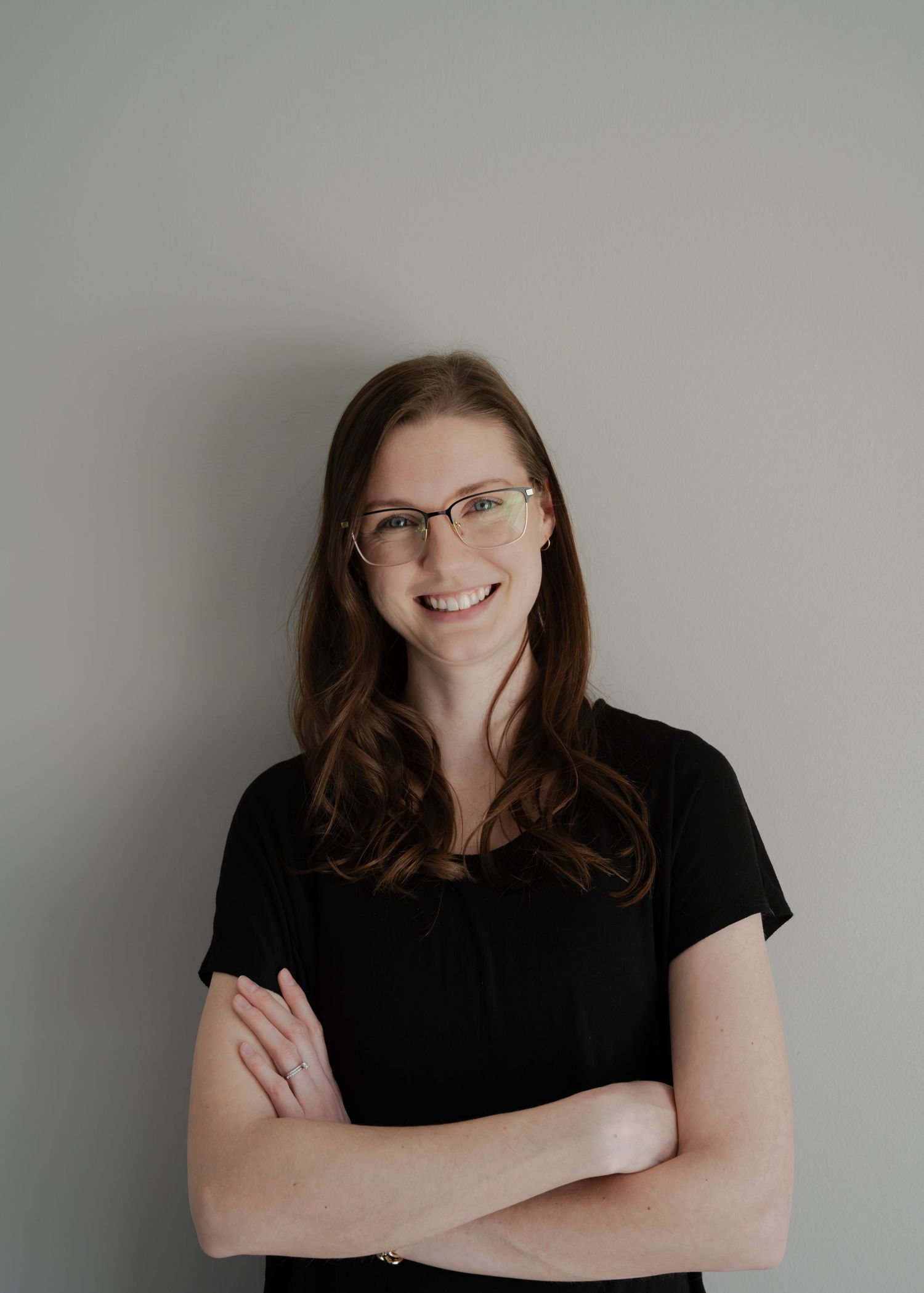 Portrait of woman with glasses and brown hair wearing black shirt with arms crossed.
