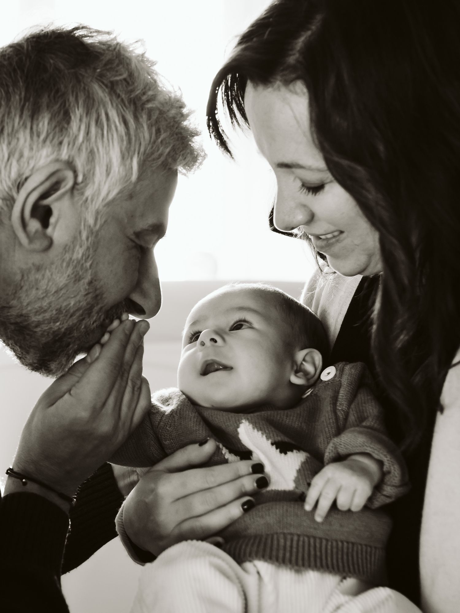 Black and white close-up of parents smiling at alert newborn baby.