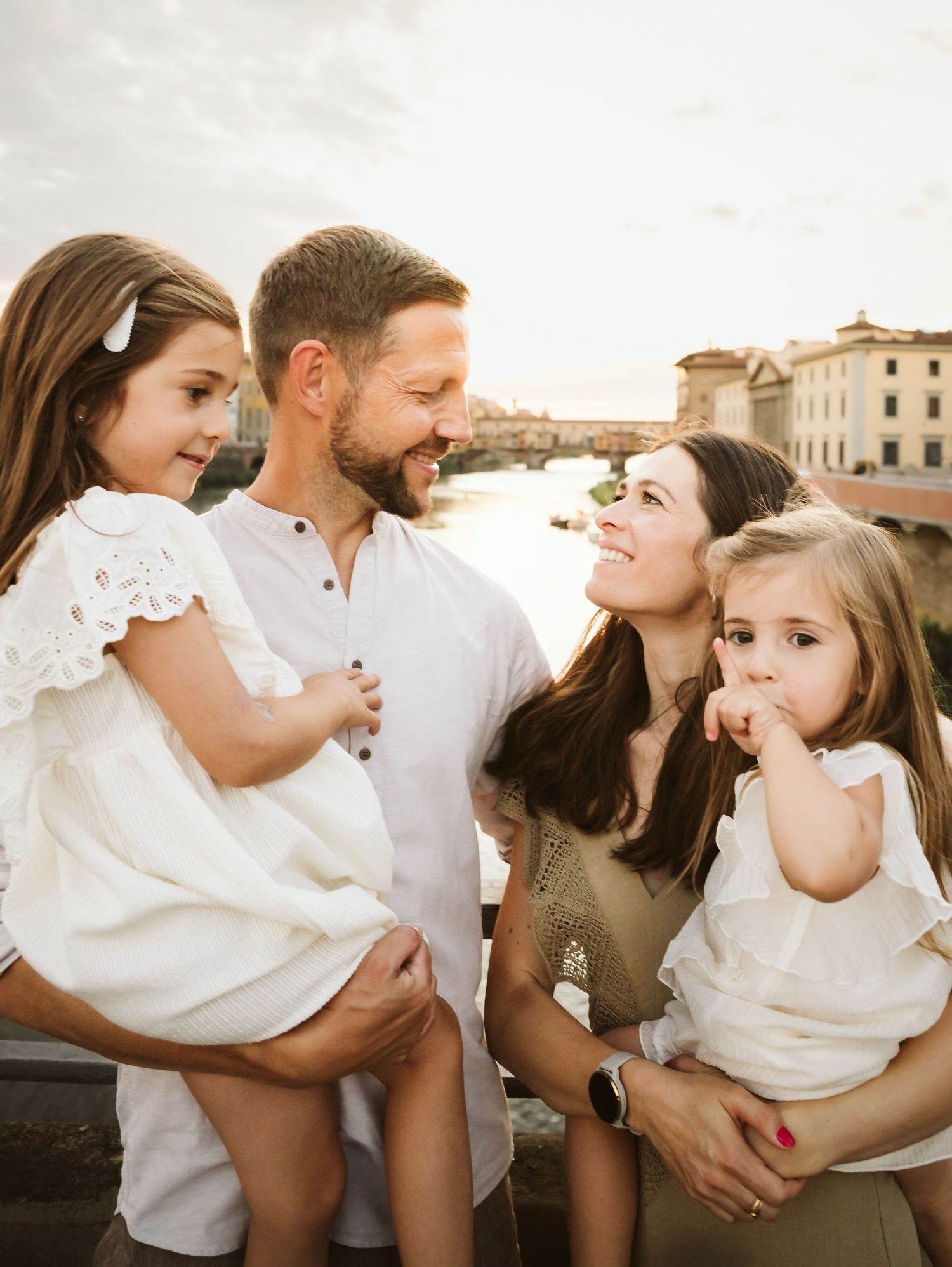 Loving family of four sharing a tender moment near the Ponte Vecchio in Florence at sunset.