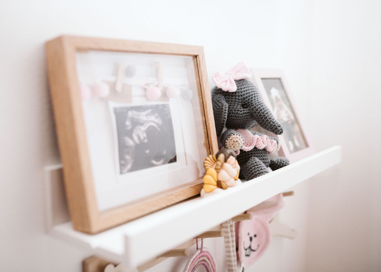 A nursery shelf displays framed baby photos and a crocheted elephant toy.