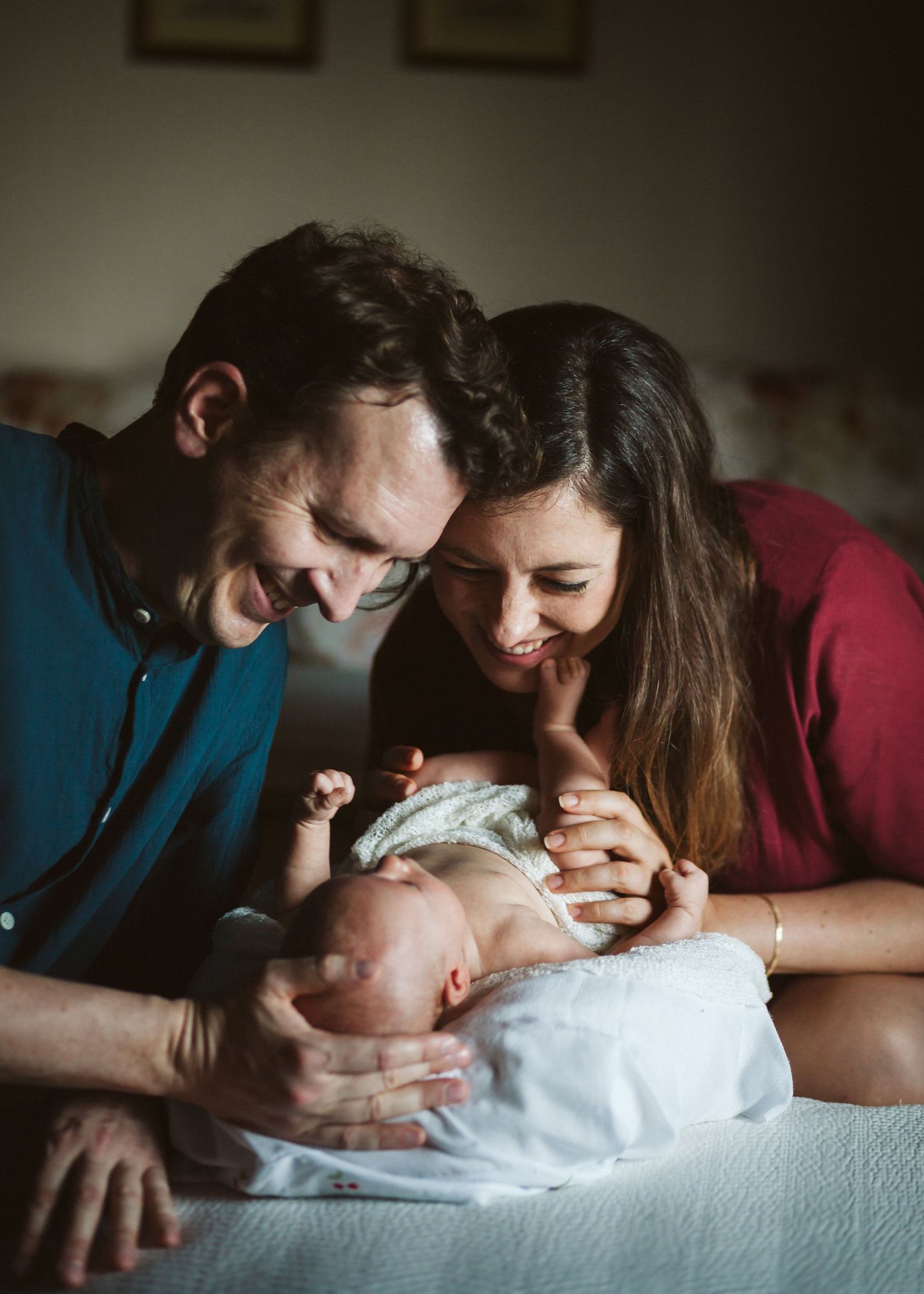 Happy couple gazing lovingly at newborn baby held on white bed.