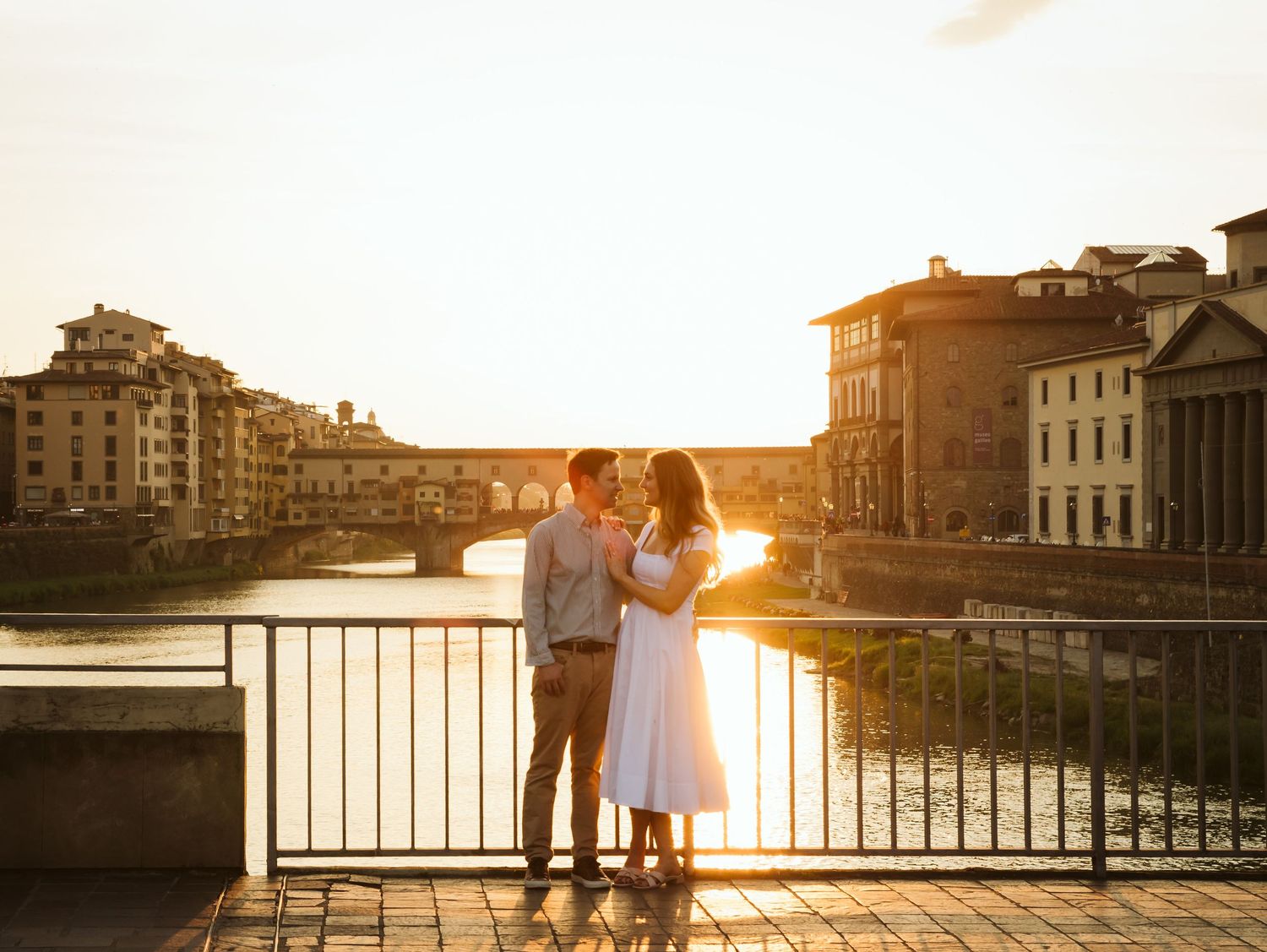 Romantic couple embracing on a bridge with Ponte Vecchio at sunset in Florence.