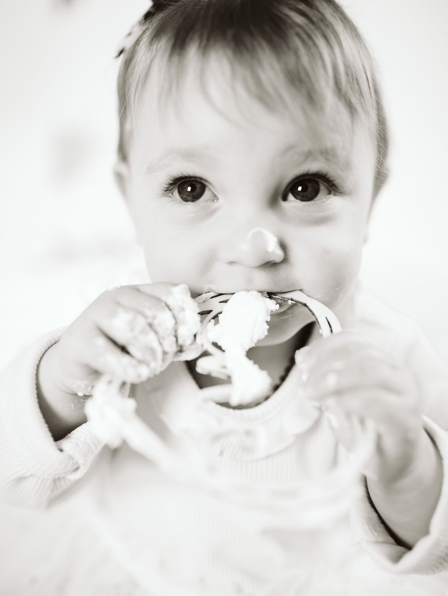A black and white portrait of a baby eating birthday cake with messy hands.